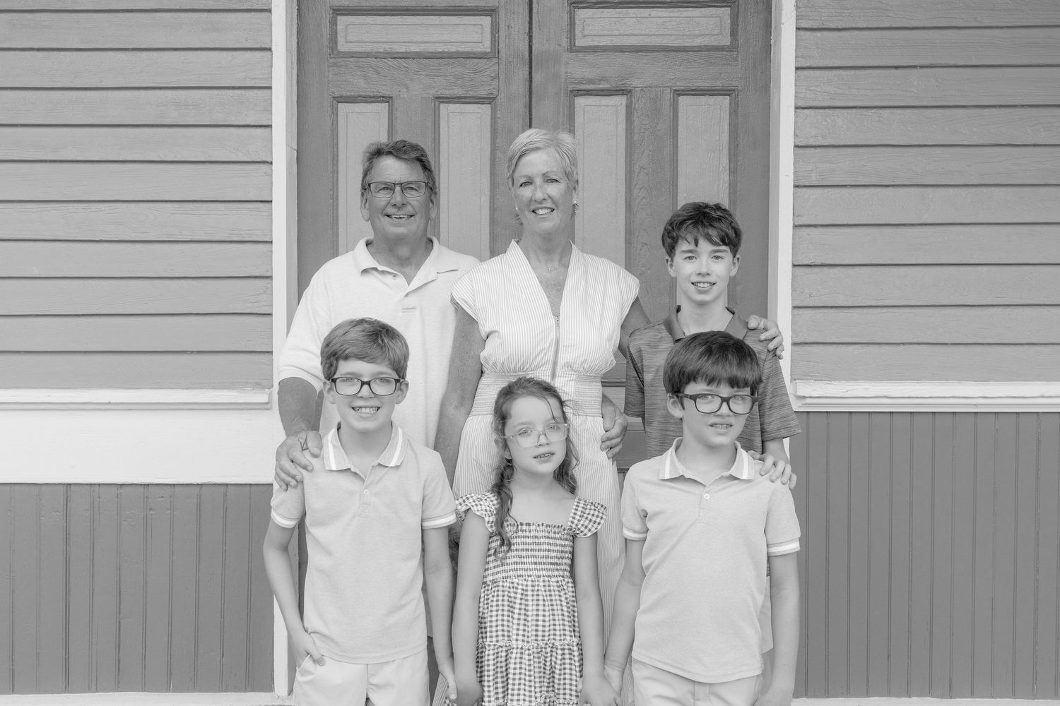 Family of six poses in black and white photo in front of a building with two adults and four children.