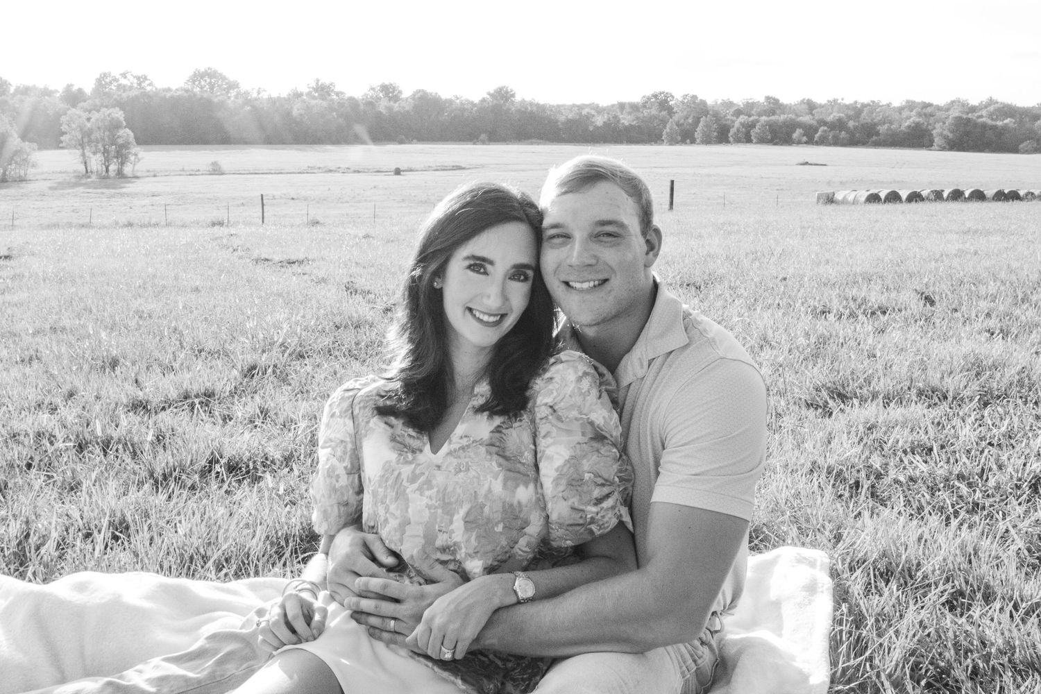 A couple poses together in a grassy field with soft natural lighting during a romantic outdoor photo session. Zach and Taylor. Gender reveal