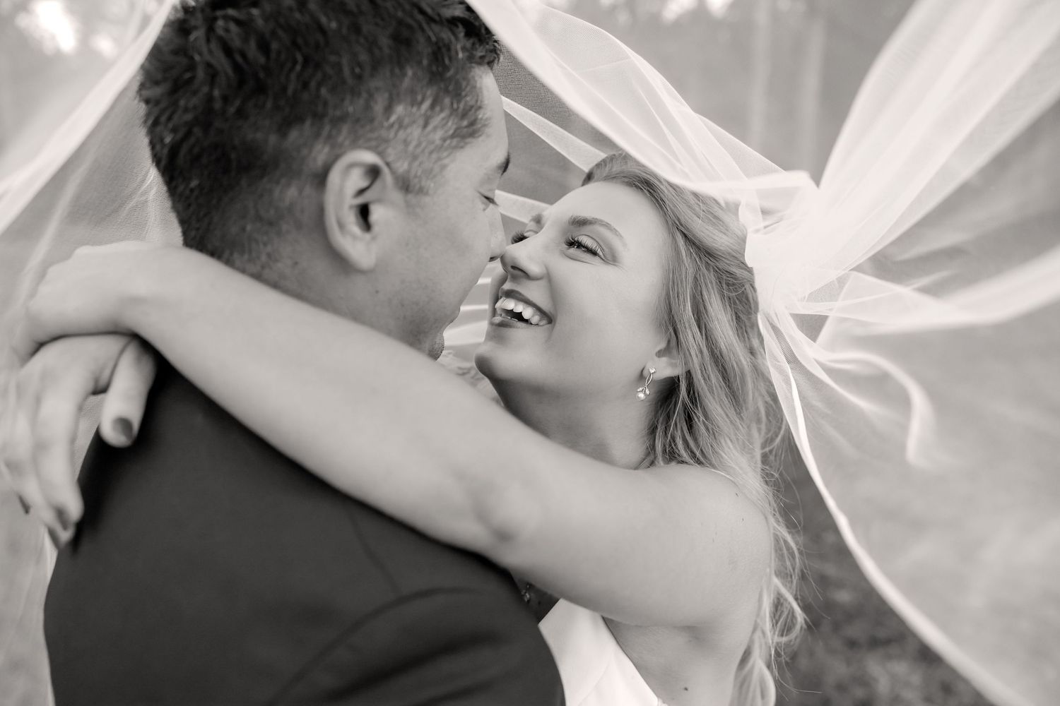 A romantic wedding photo series showing tender moments between a couple embracing under white fabric draping.