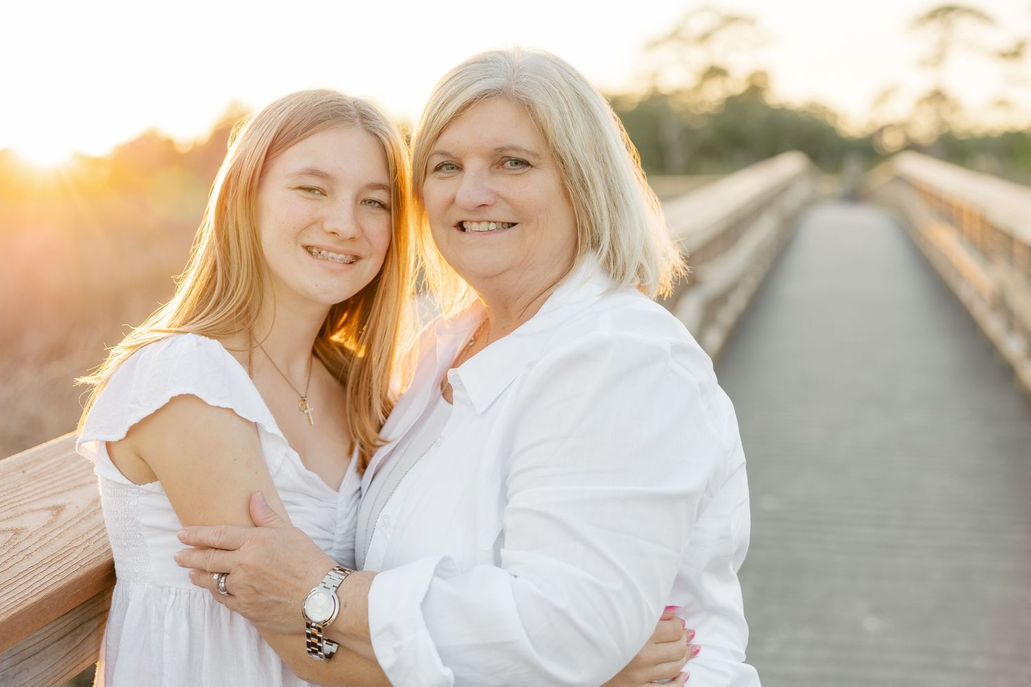 A mother and daughter share tender moments walking along a wooden boardwalk at sunset.