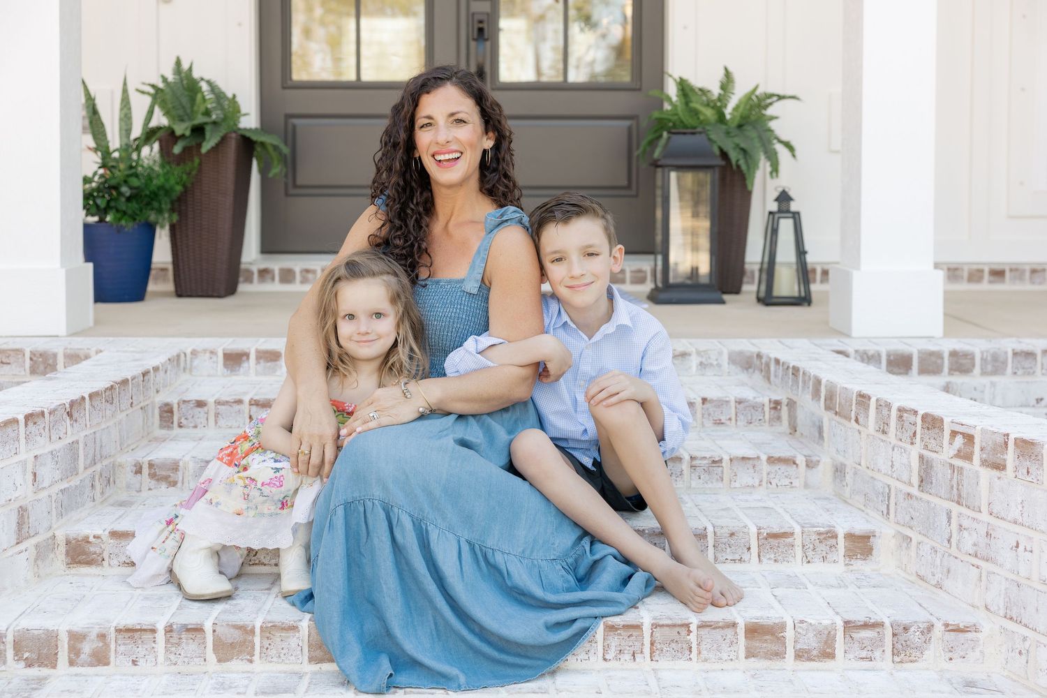 Mother with two young children sitting on brick porch steps of elegant white home.