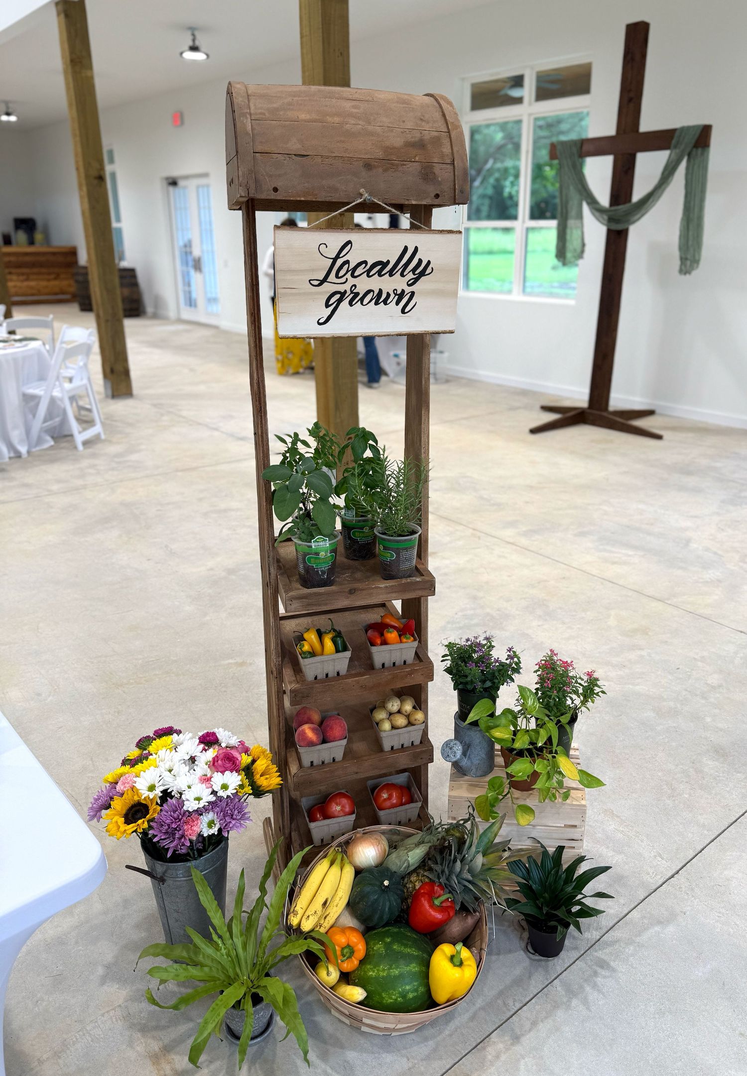 Rustic wooden market stand display with fresh produce, plants and flowers arranged in tiers.