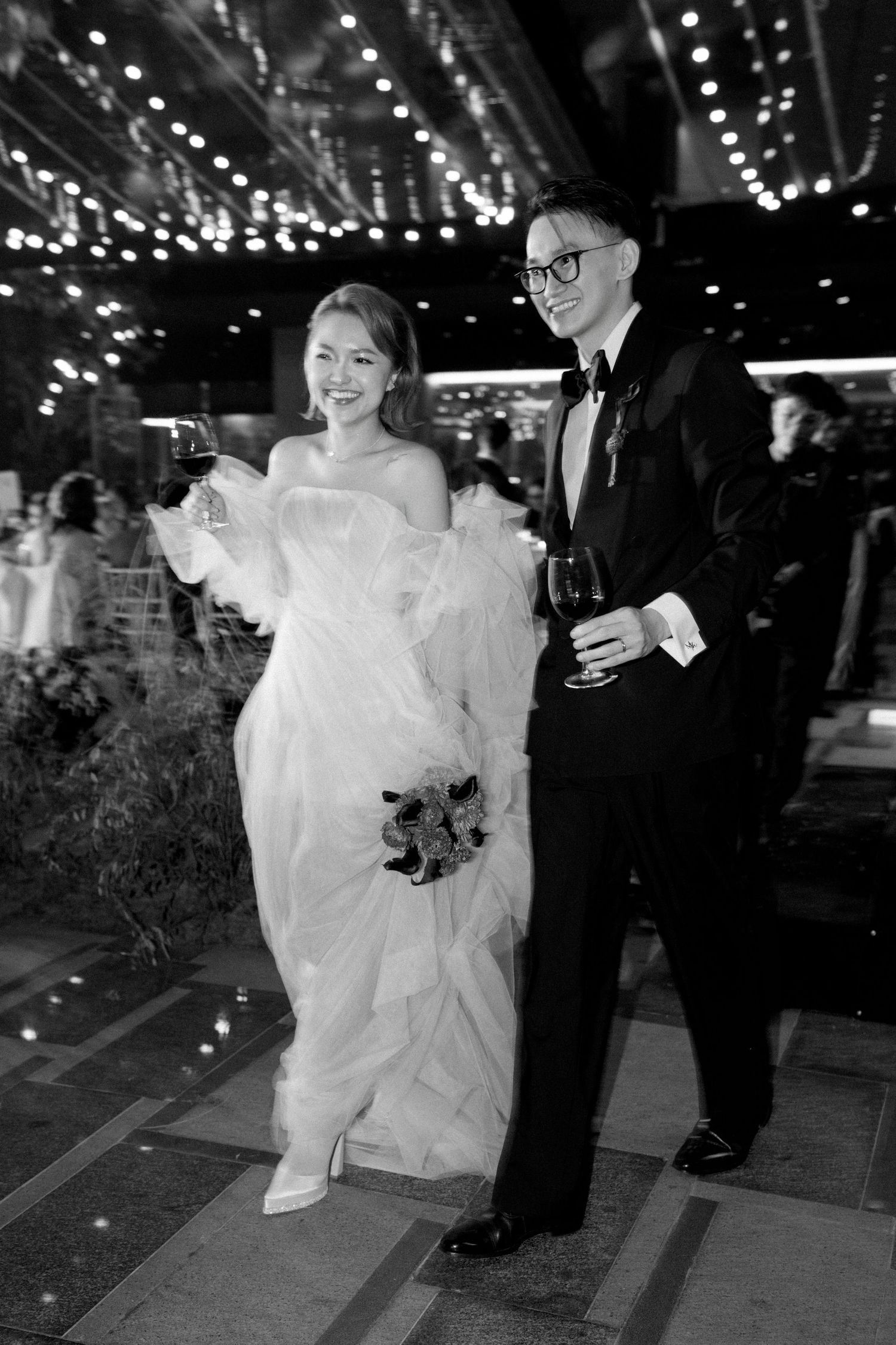 A bride in a white wedding dress and groom in dark suit dance together under twinkling lights at their reception.