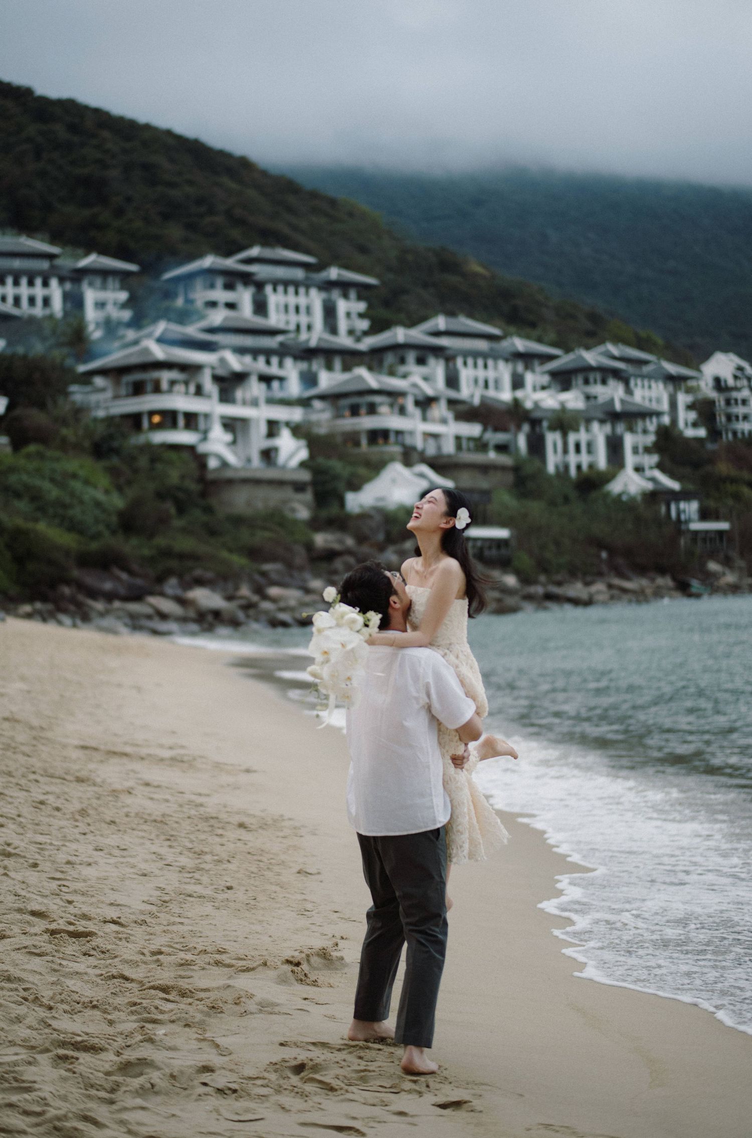 A romantic scene on a beach with luxury hillside buildings in the background.