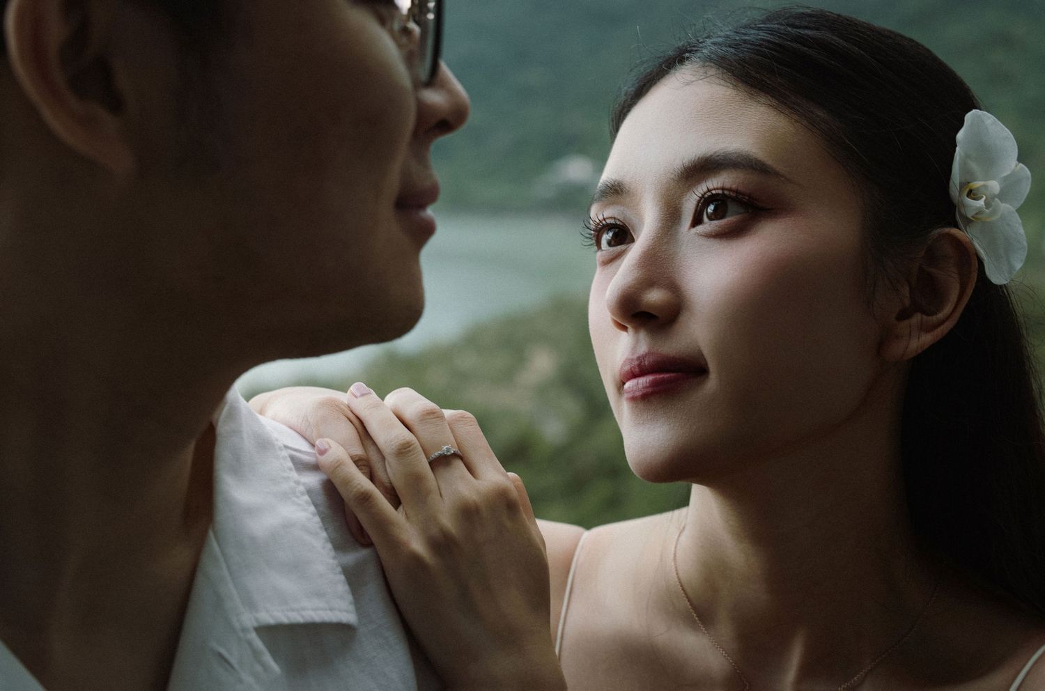 An intimate close-up portrait with soft lighting and natural scenery in the background.