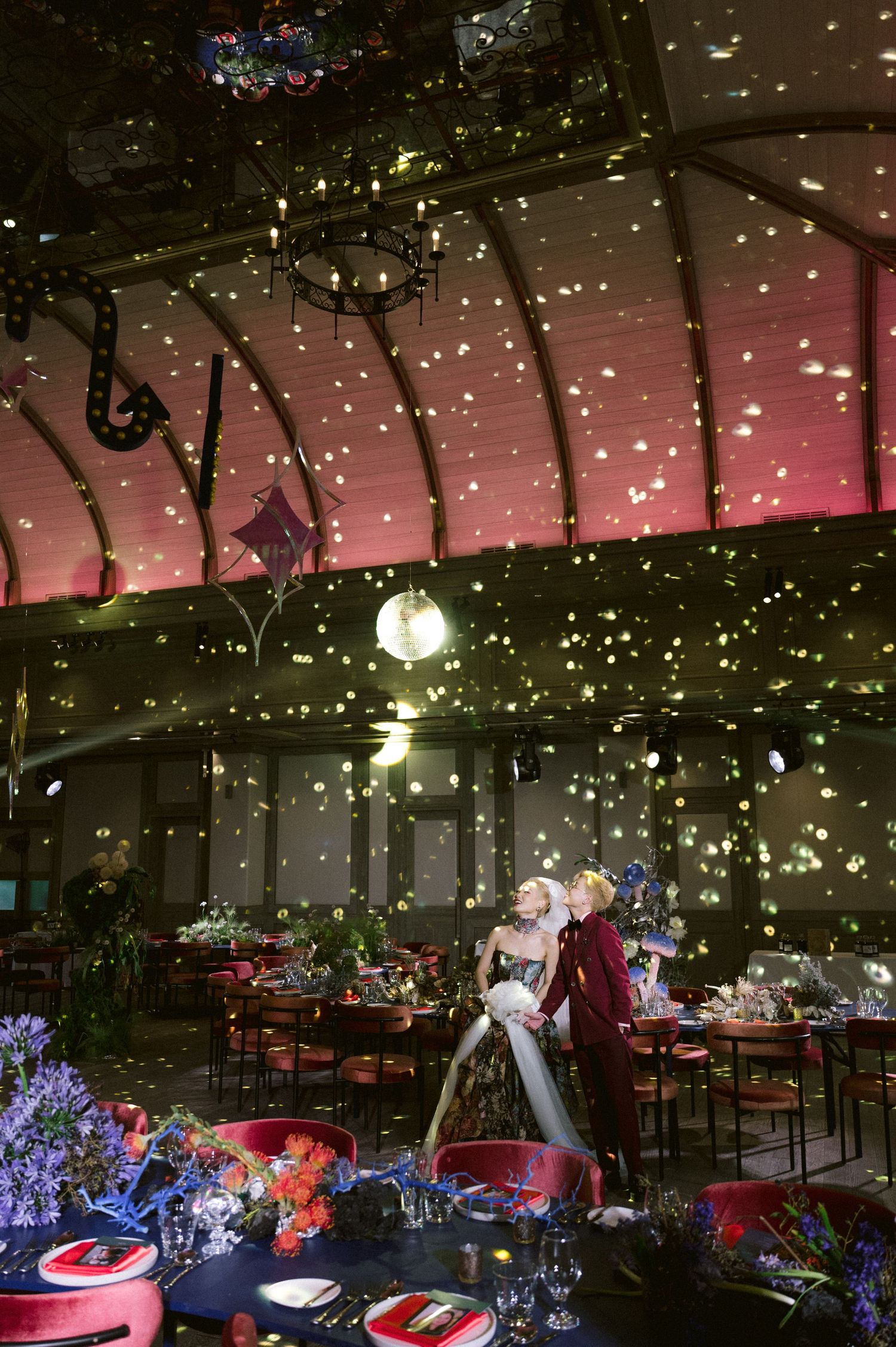 Elegant wedding reception venue with twinkling lights, floral arrangements and romantic evening ambiance under a glass ceiling.