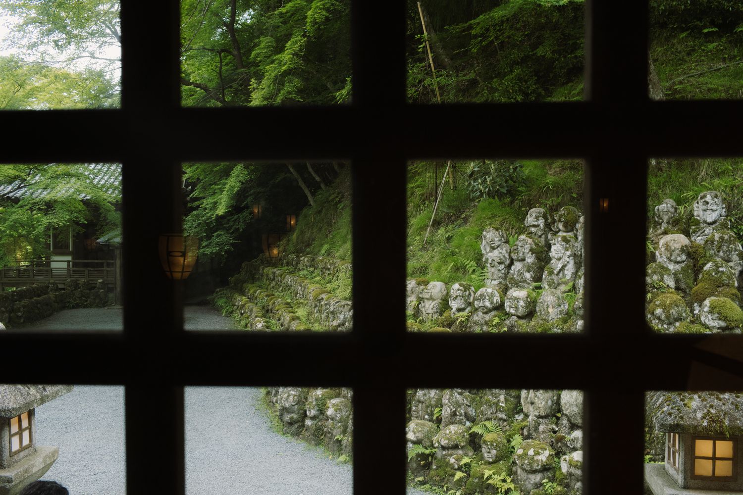 A serene Japanese garden pathway bordered by lush greenery and traditional wooden architecture and fencing.