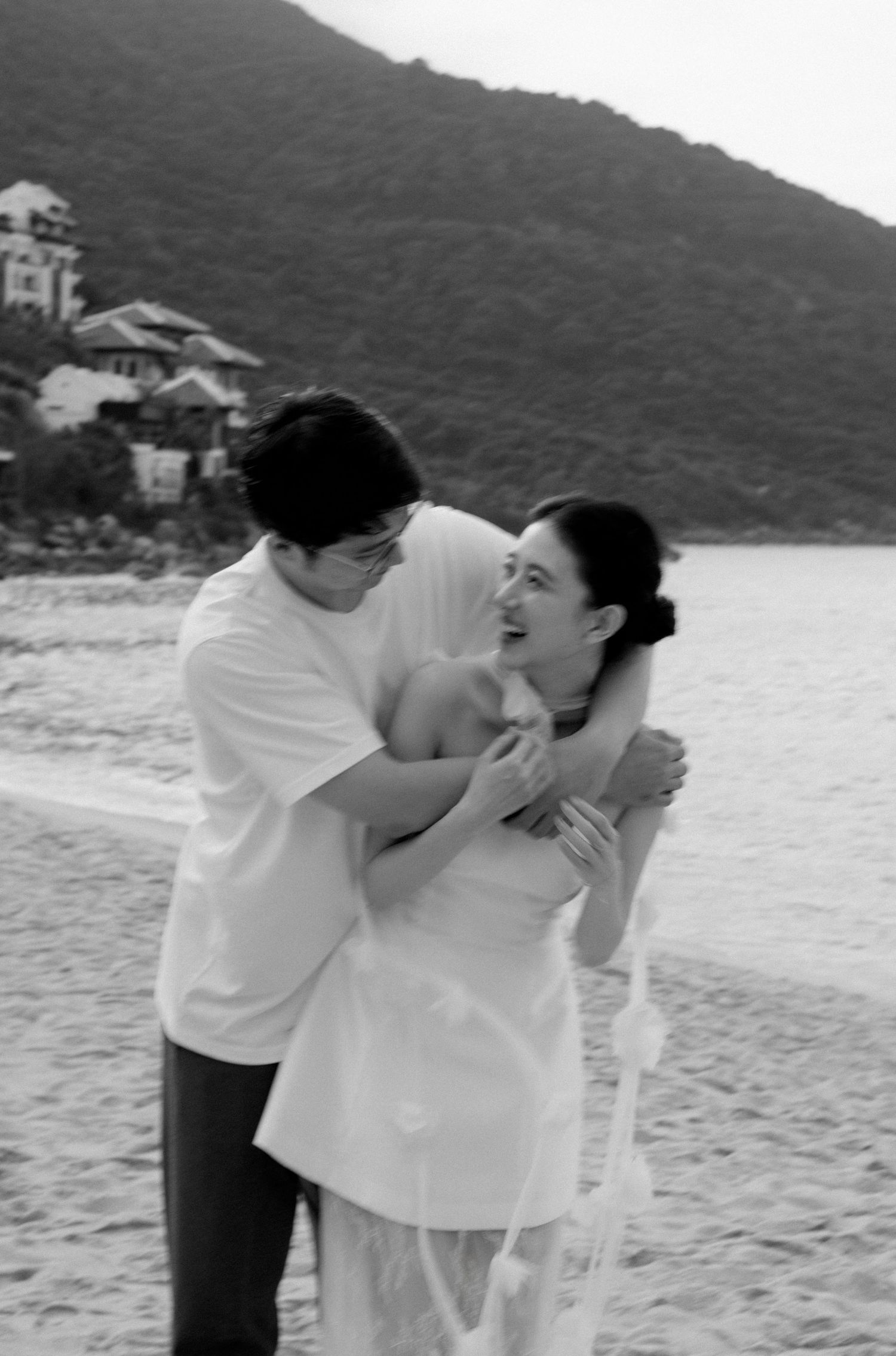 A joyful moment captured in black and white on a scenic beach with mountains visible.