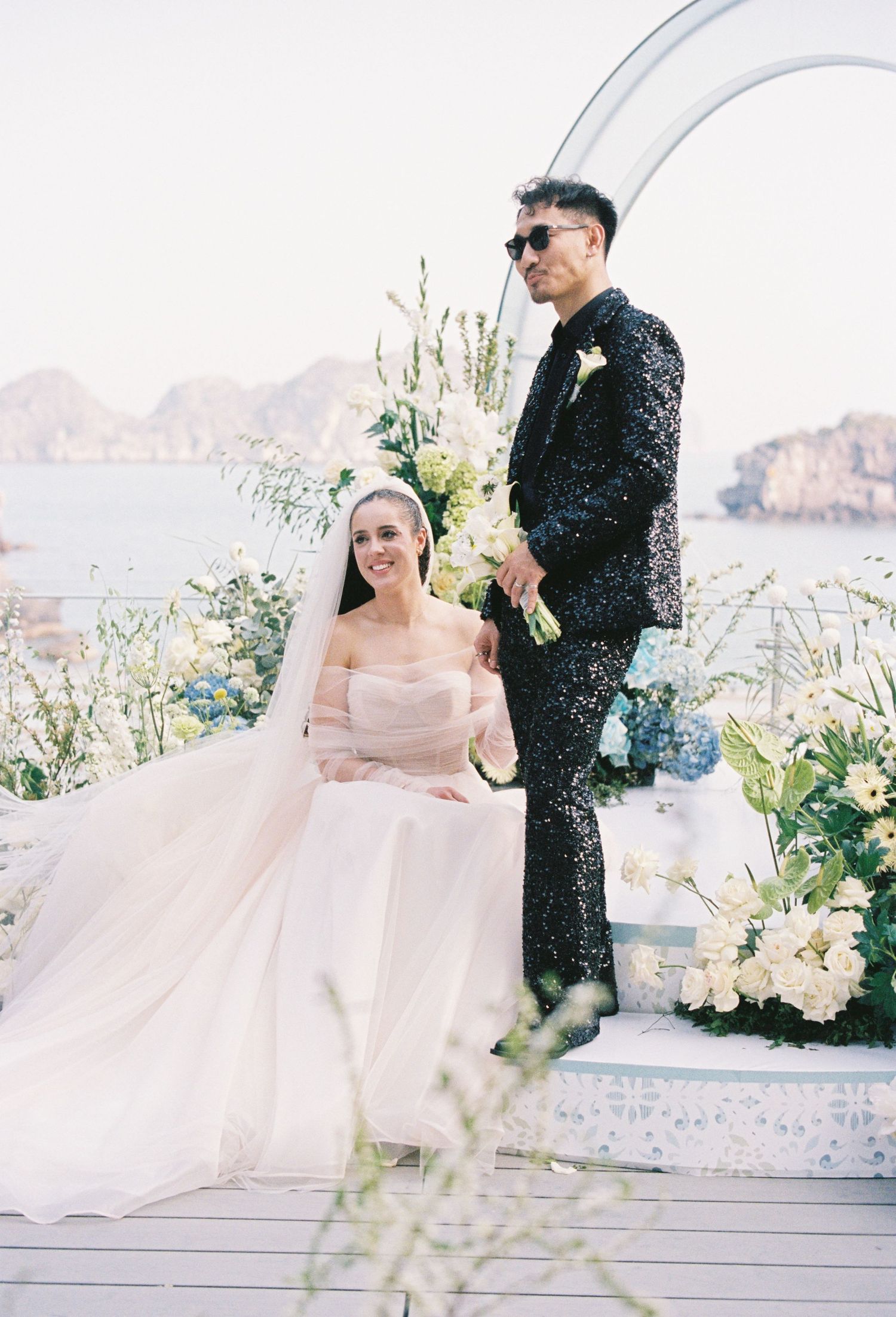 A couple celebrates their wedding day in an elegant outdoor setting overlooking mountains and floral arrangements.
