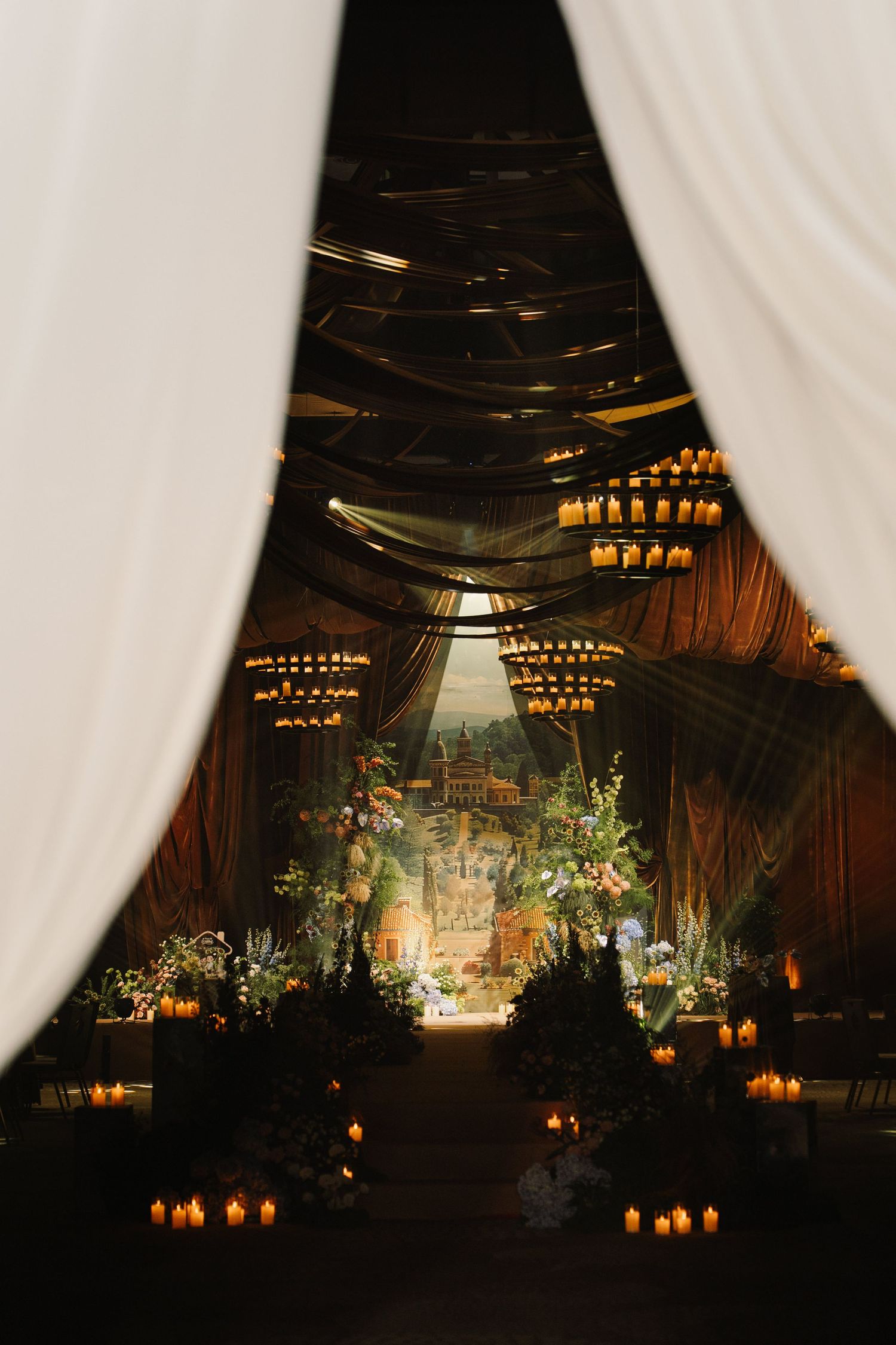 Elegant wedding venue interior with dramatic lighting, chandeliers, and white draping creating a romantic atmosphere.