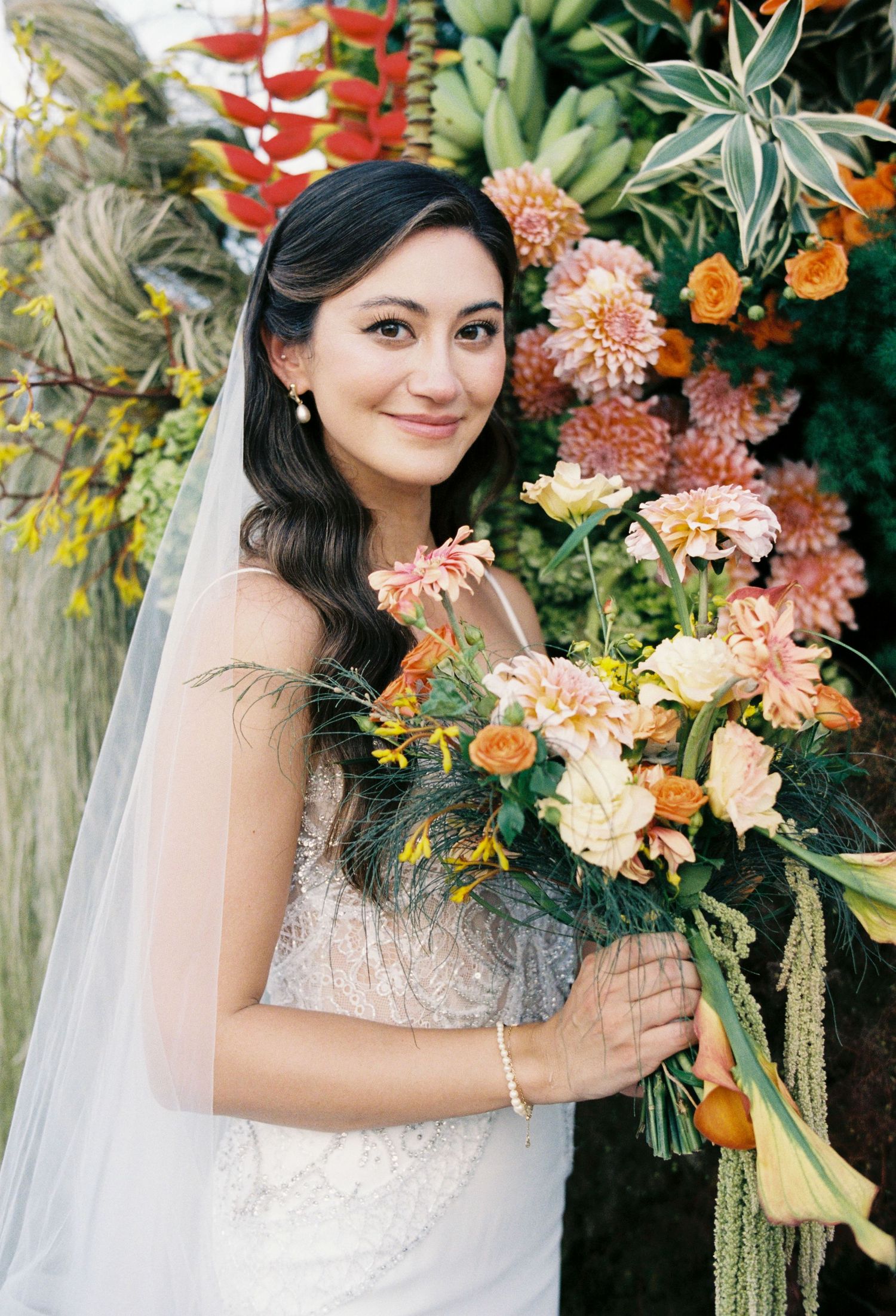 A bride holds a lush peach and coral bouquet with cascading greenery against a floral backdrop in a series of photos.
