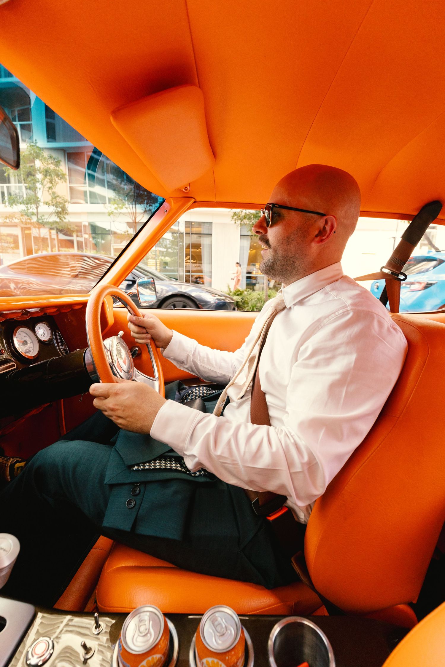 Person in white shirt driving vintage car with bright orange interior.