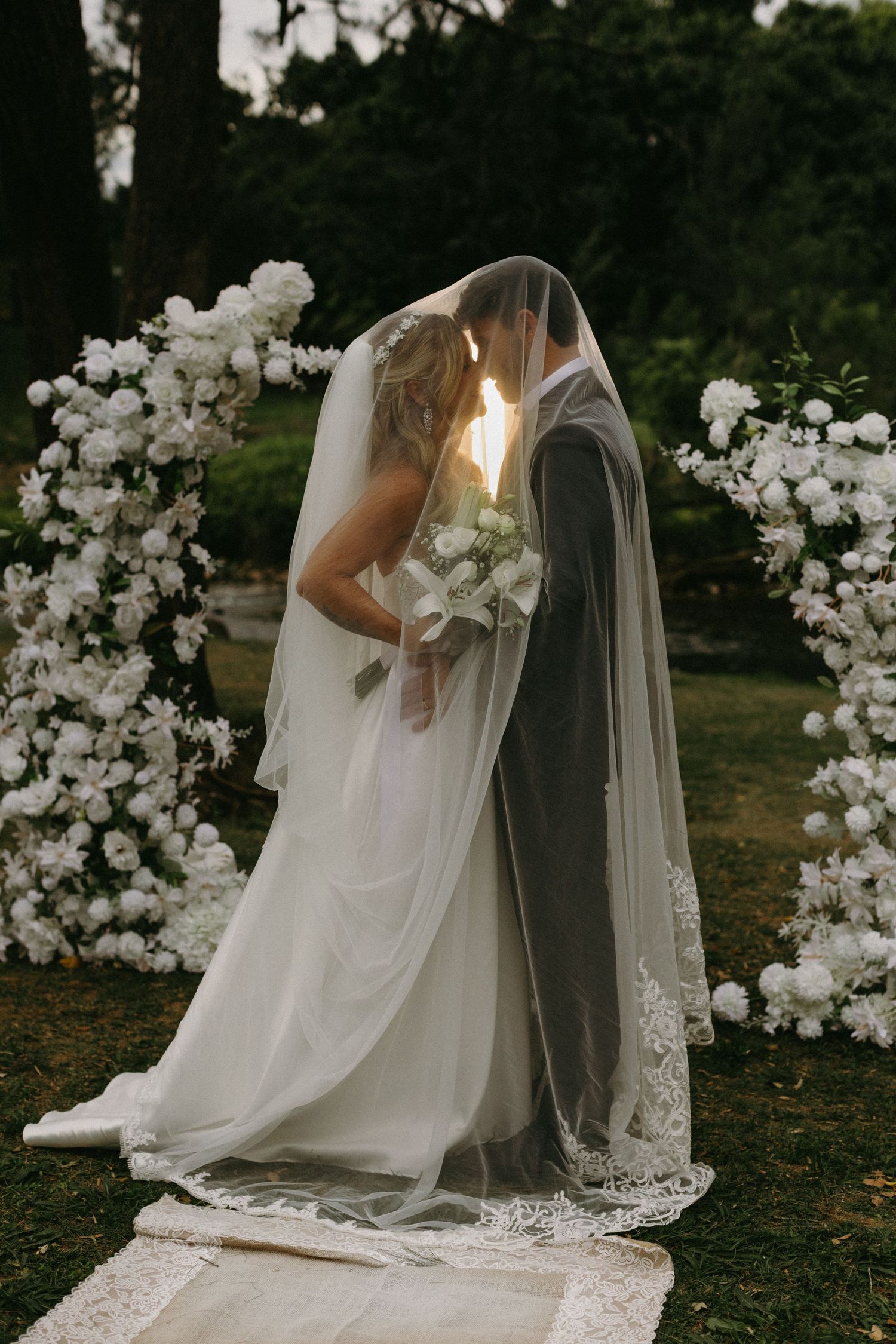 Elegant white floral wedding arch with delicate lace veil details.