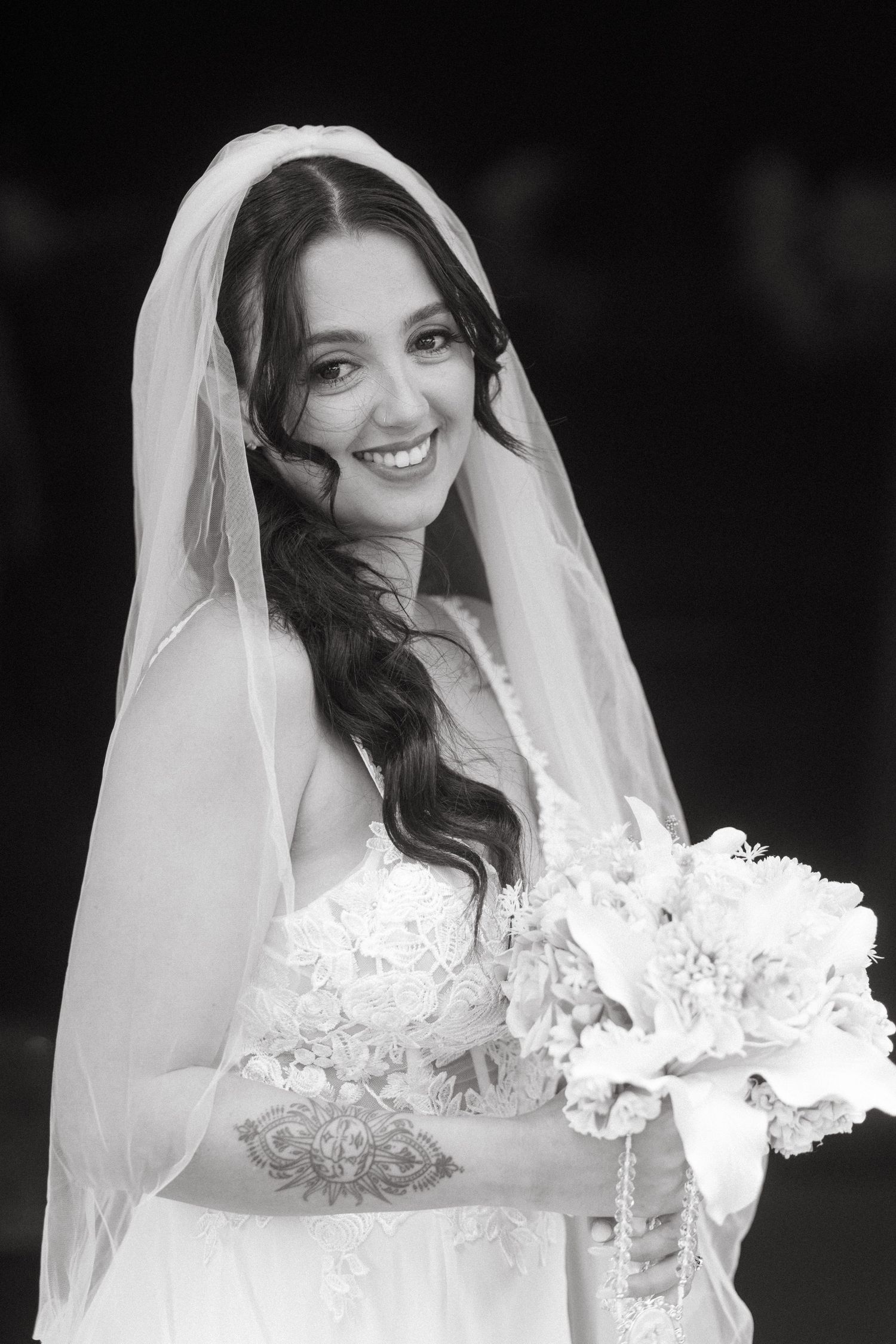 A bride in a white lace wedding dress and veil poses with her bouquet.
