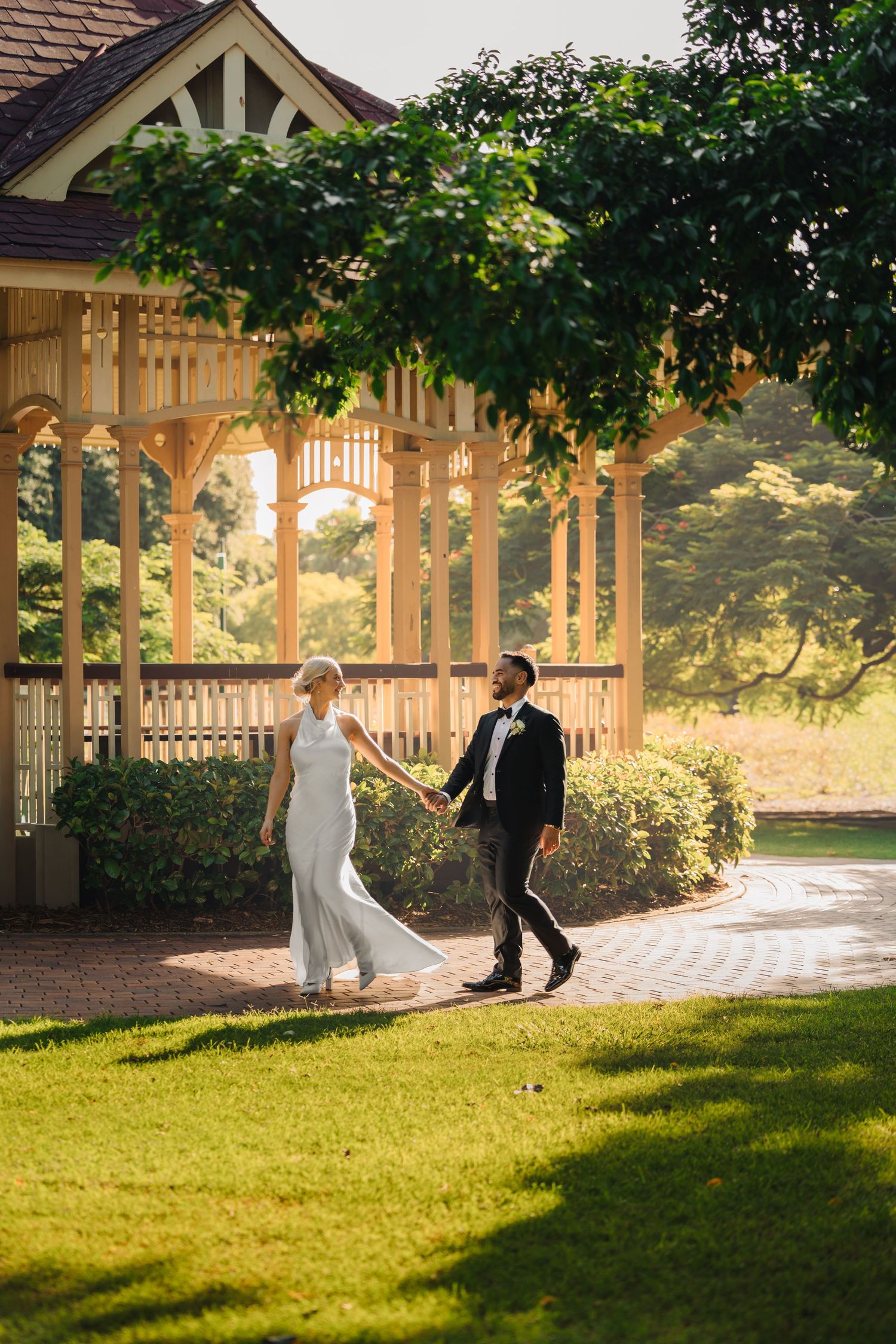 A couple dances together in a sunlit wooden gazebo surrounded by lush greenery on a summer afternoon.