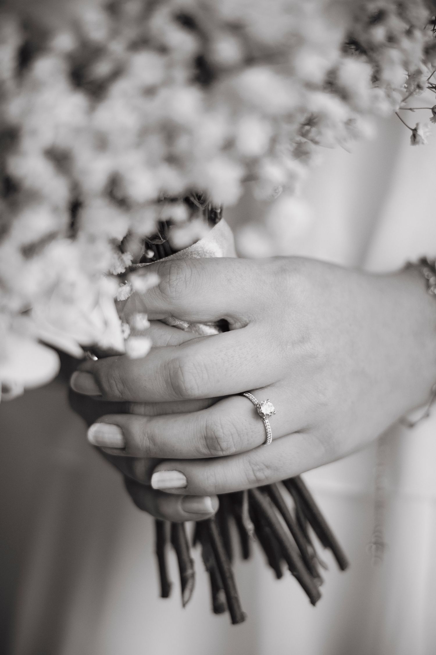 Black and white close-up shots of hands with an engagement ring holding delicate spring blossoms.