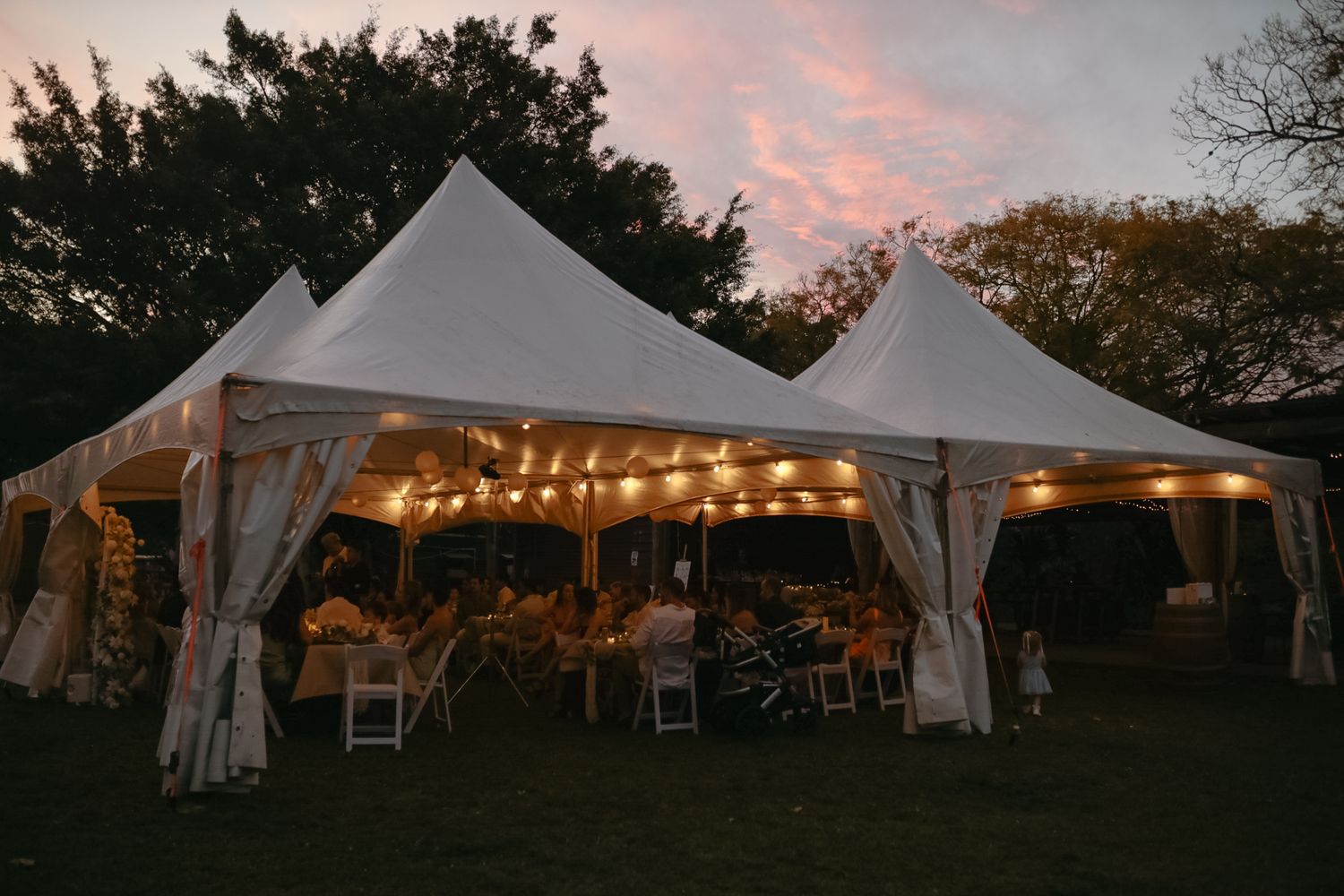 Wedding reception tent setup at sunset with string lights and outdoor seating.