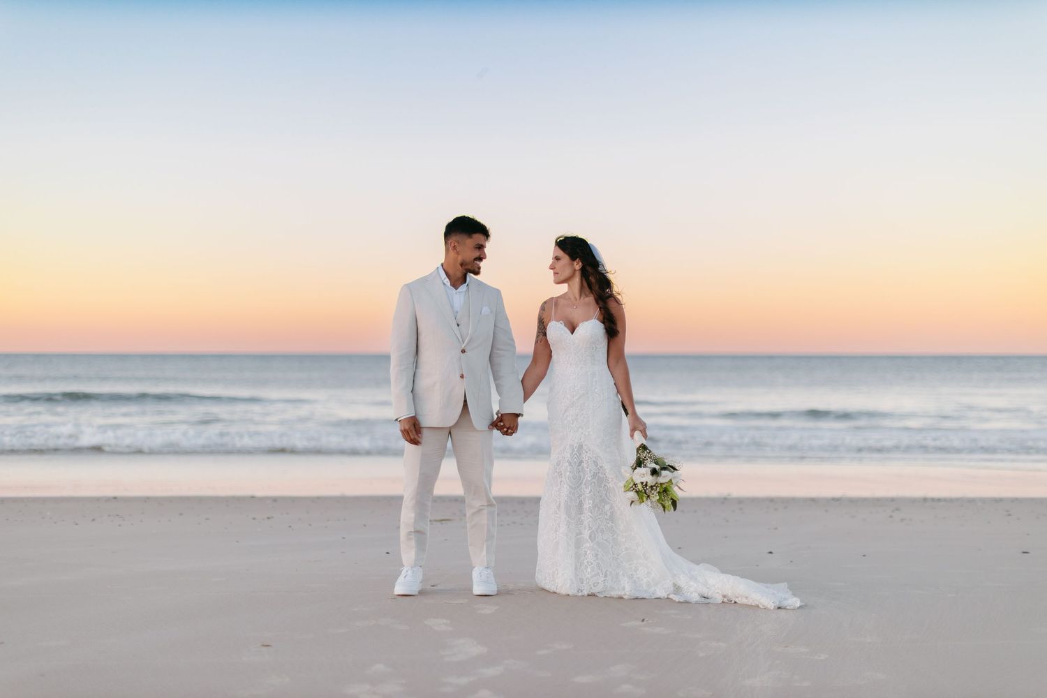 A romantic beach wedding scene at sunset with the couple walking along the shoreline.