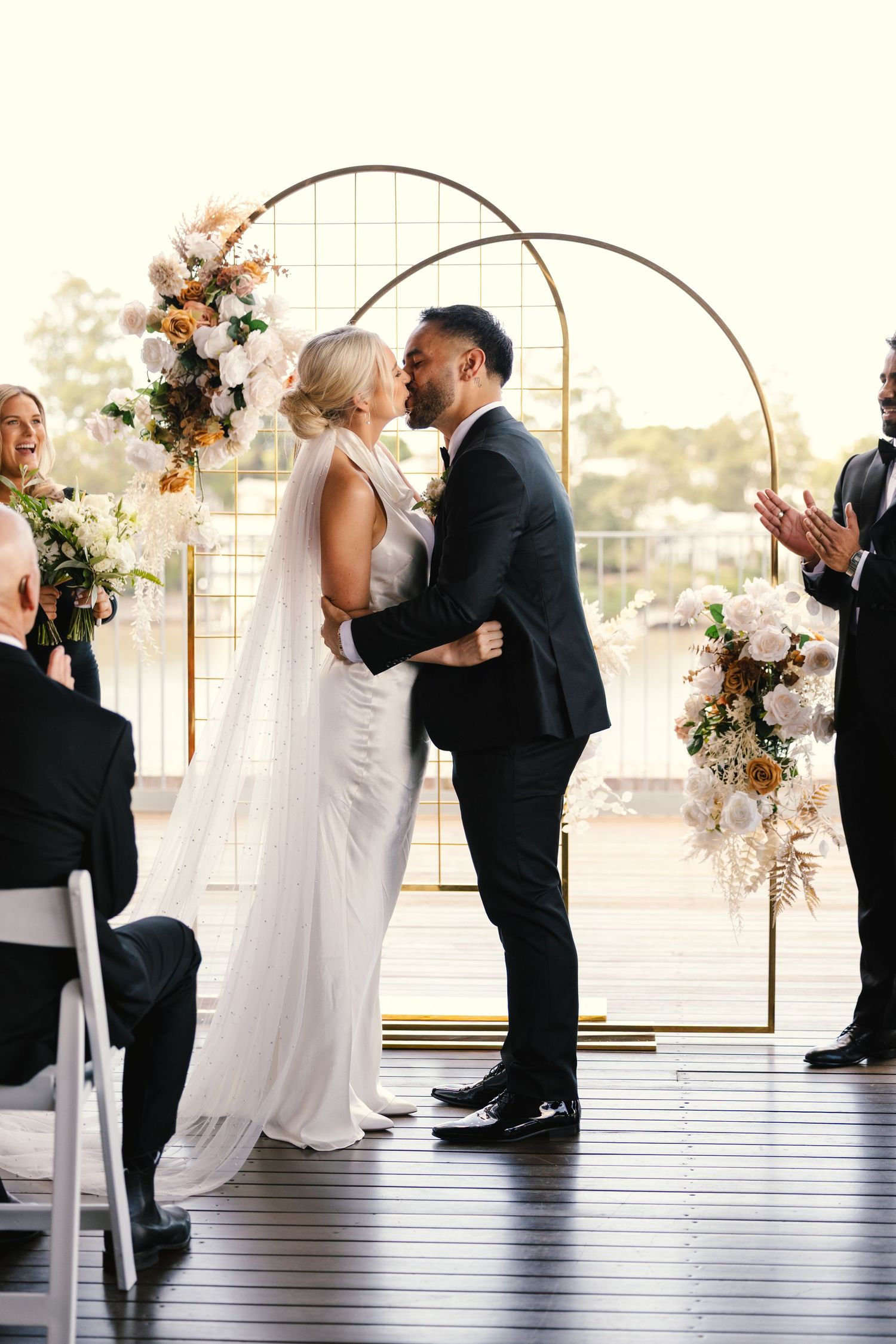 Couple shares their first kiss under a floral arch during wedding ceremony.