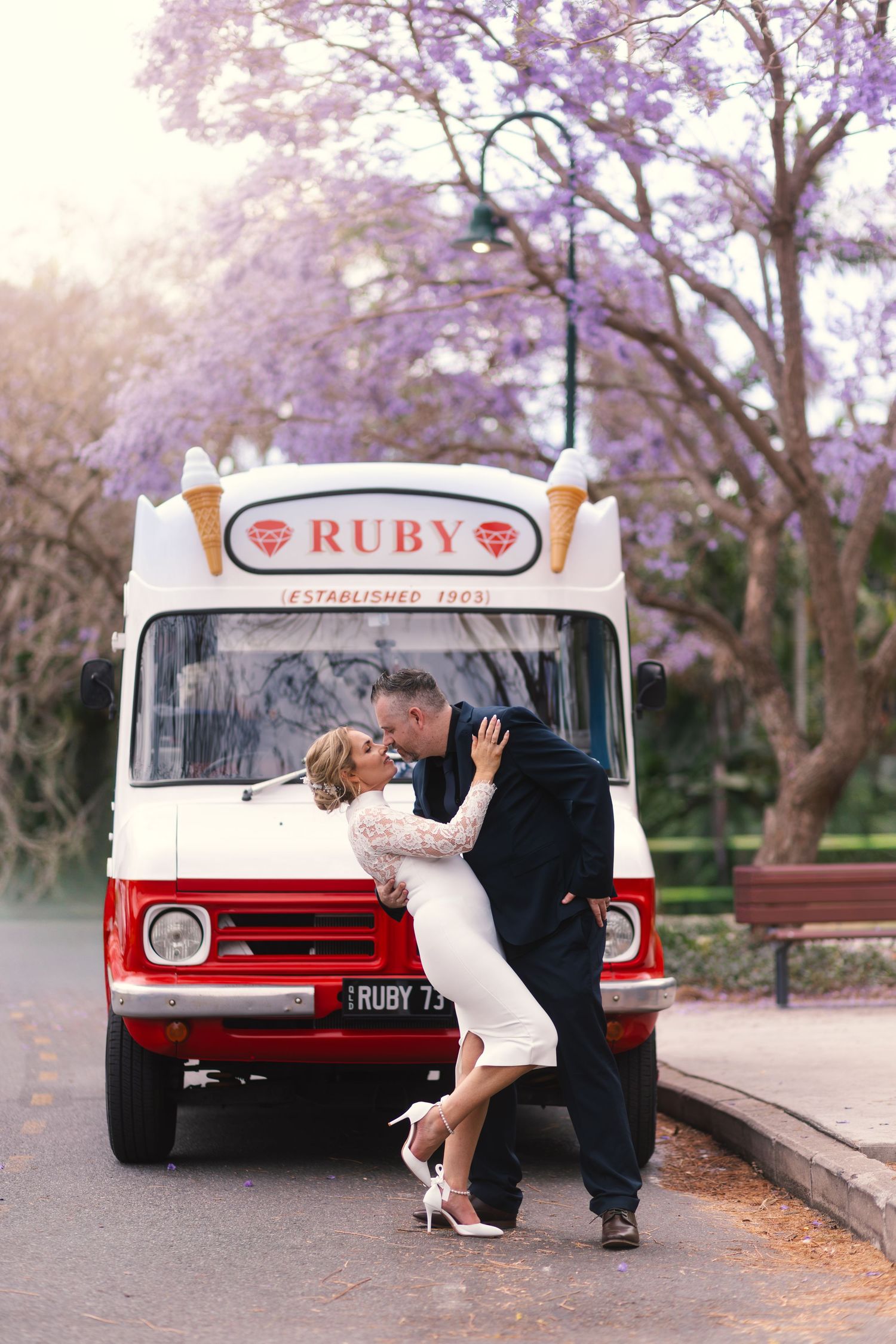 Romantic couple poses near vintage red and white Ruby bus during outdoor photo session.
