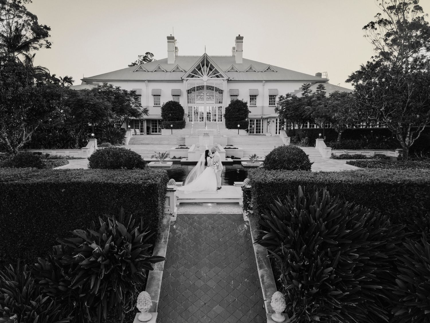 Historic mansion with formal gardens and pathway leading to grand white building with columns and symmetrical architecture.