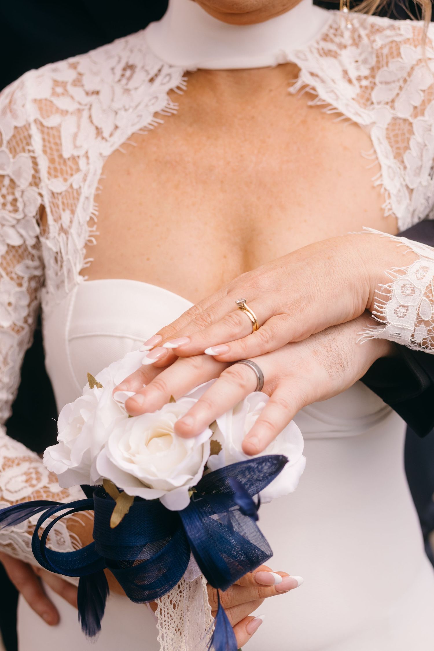 Close-up detail of hands holding a navy blue silk ribbon against a white wedding dress with delicate lace sleeves.