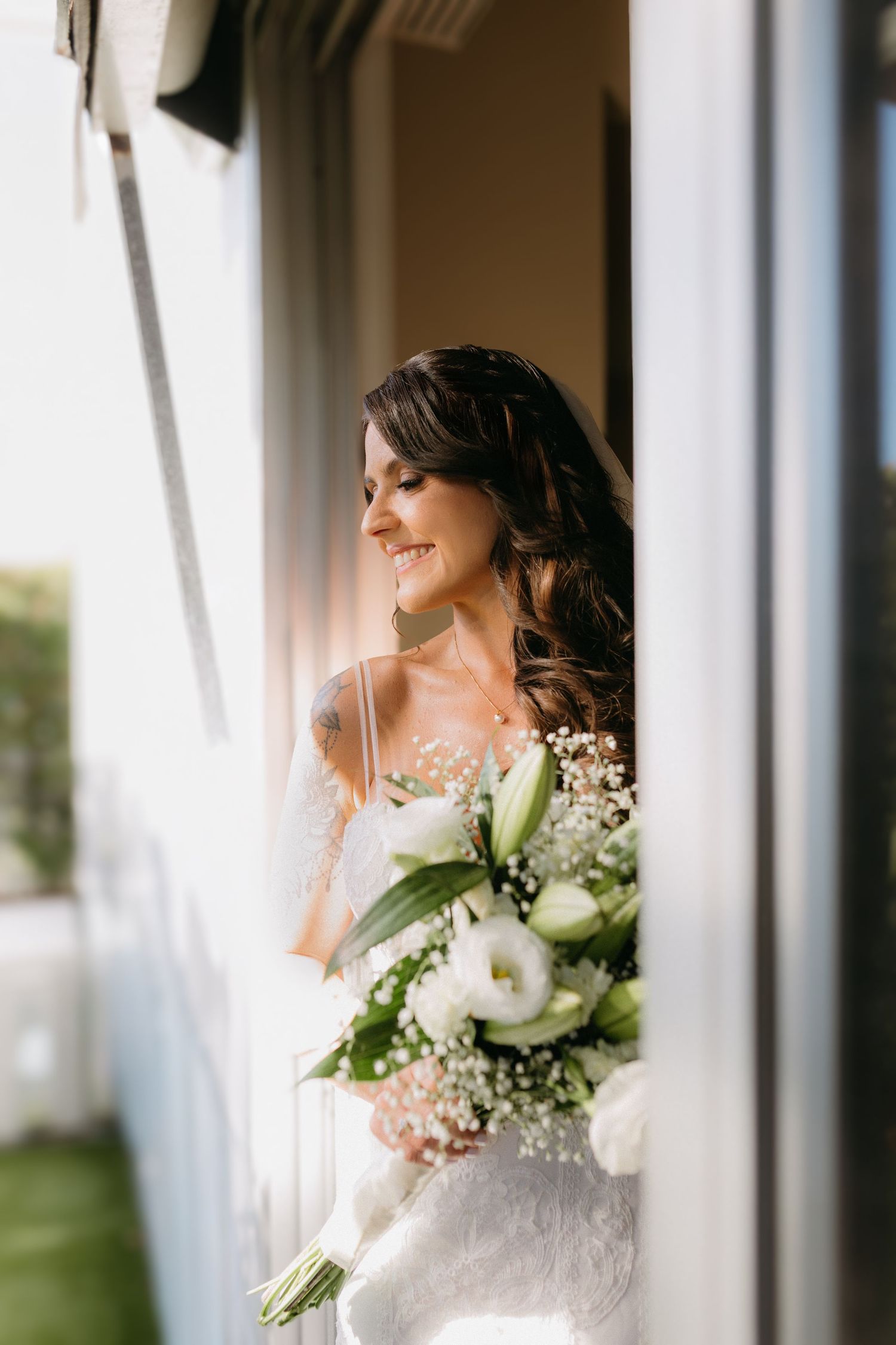 A side profile portrait of a bride holding a white and green bouquet near sunlit windows.