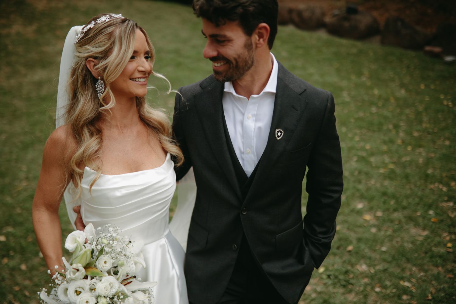 Elegant wedding couple sharing a romantic moment on a grassy lawn in formal attire.