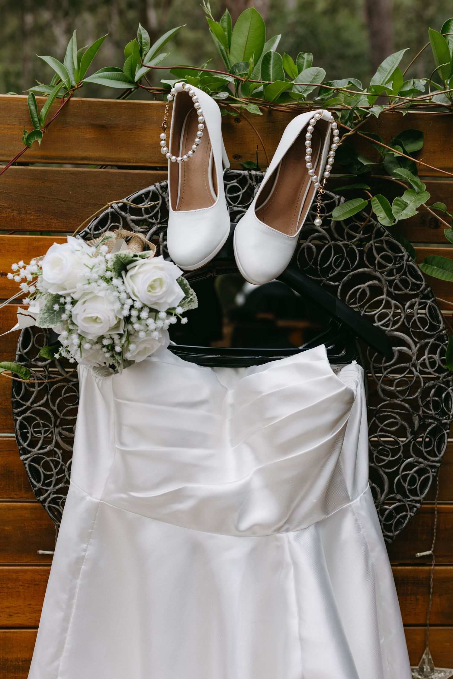 White wedding dress and bridal shoes displayed with floral decorations on wooden backdrop.