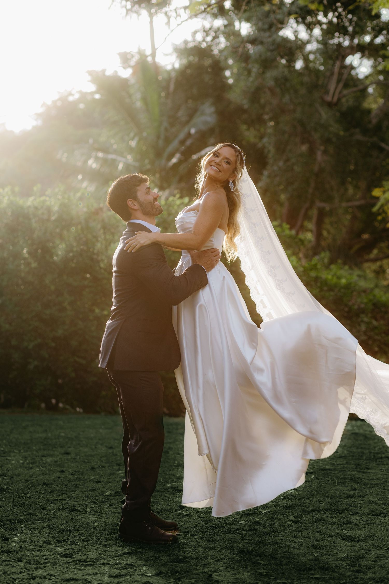A romantic wedding moment captured at sunset with a flowing white dress and veil against a lush garden backdrop.
