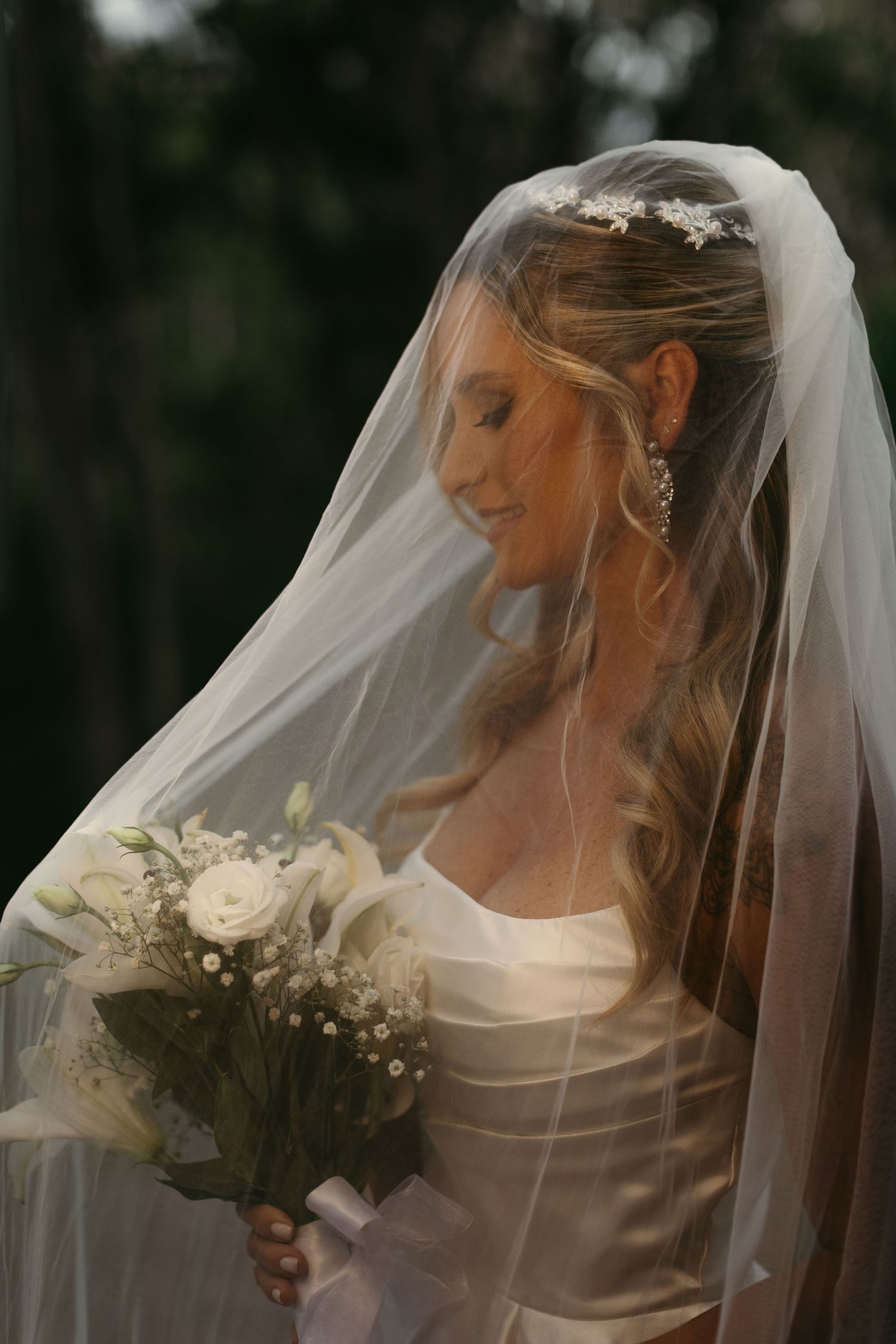 Side profile of bride with flowing veil holding white bouquet.