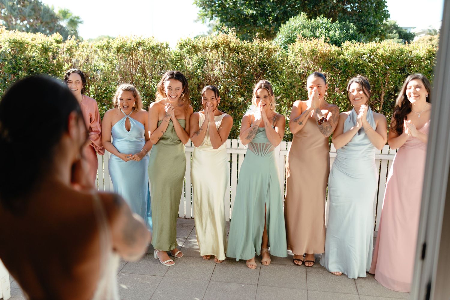 Wedding party in pastel dresses lined up outdoors for group photo.
