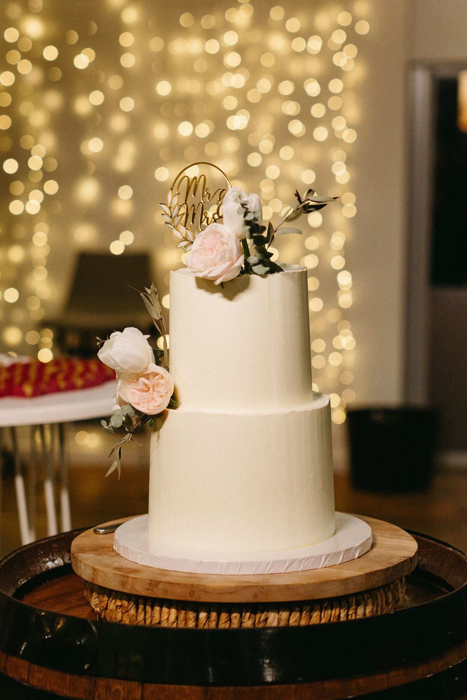 Elegant white wedding cake with floral decorations displayed against bokeh light background.