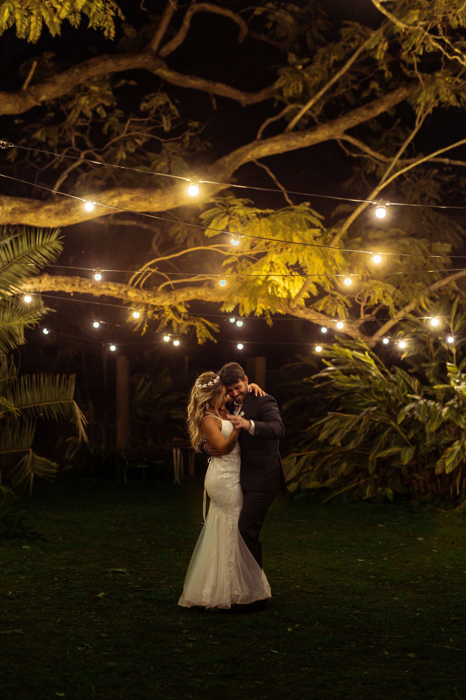 A romantic evening dance scene under string lights and palm trees in a garden setting.