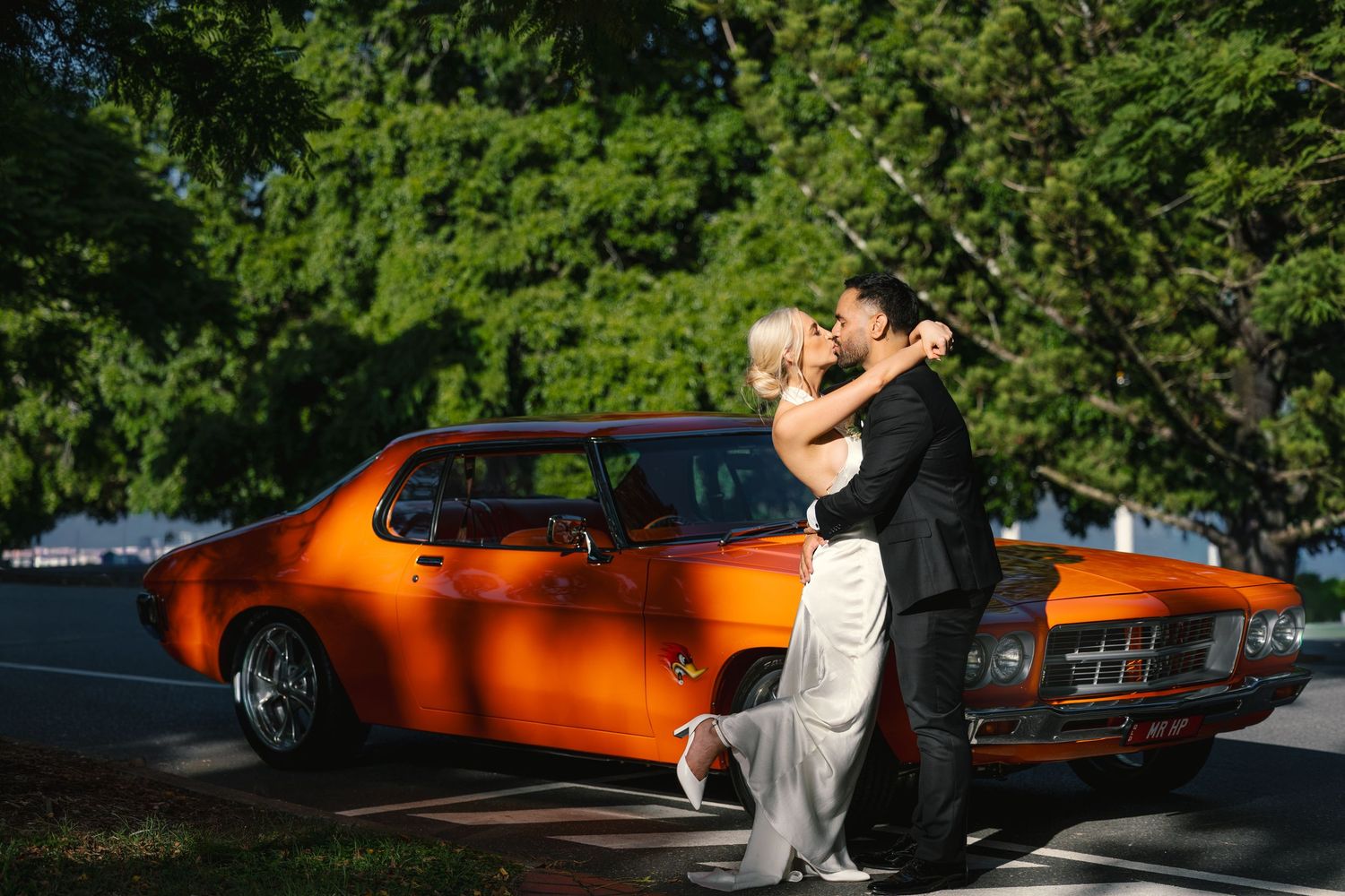 A vintage orange Pontiac GTO muscle car parked in a sunny outdoor setting with trees in the background.