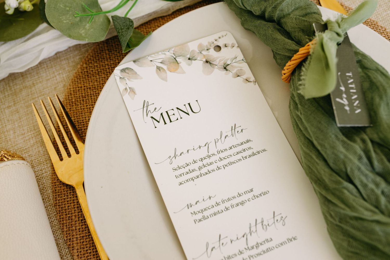 Elegant wedding menu card with floral design details placed on table setting with gold flatware and greenery.