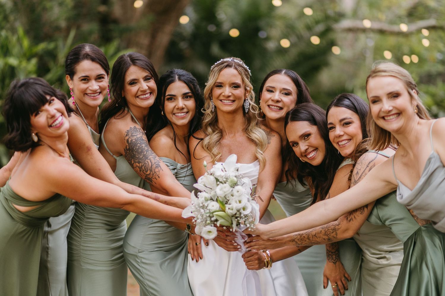 Bridal party in sage green dresses poses together with joyful expressions outdoors.