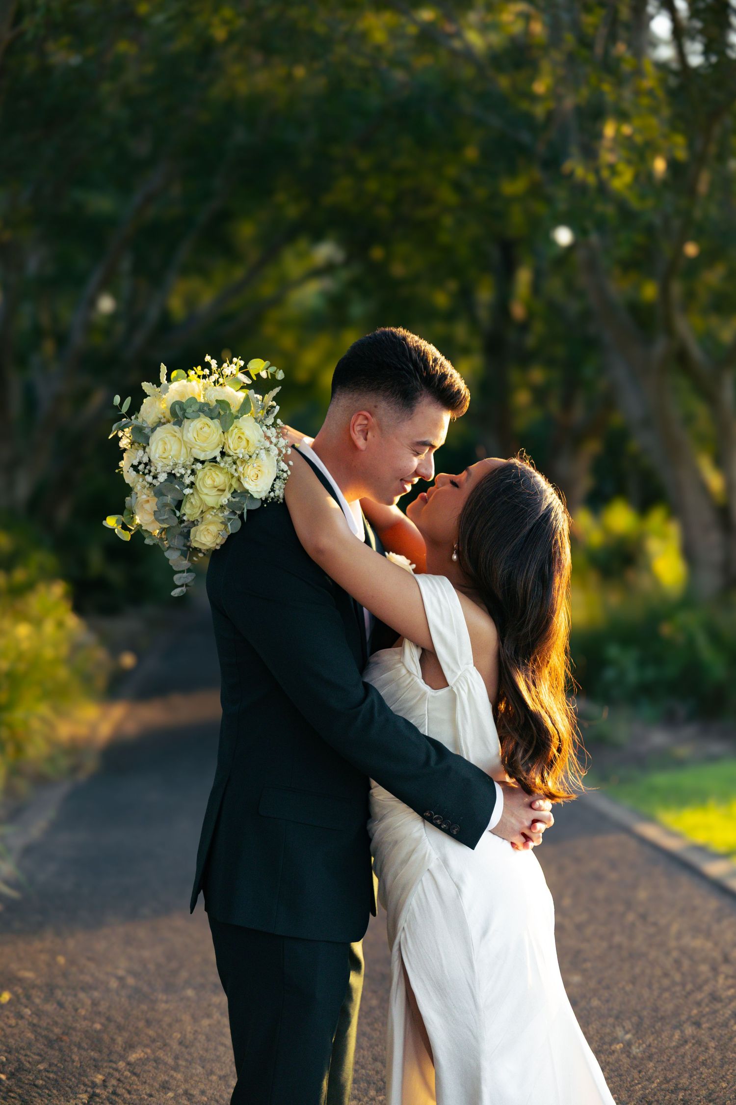A couple in wedding attire shares an intimate moment at sunset in a garden setting.