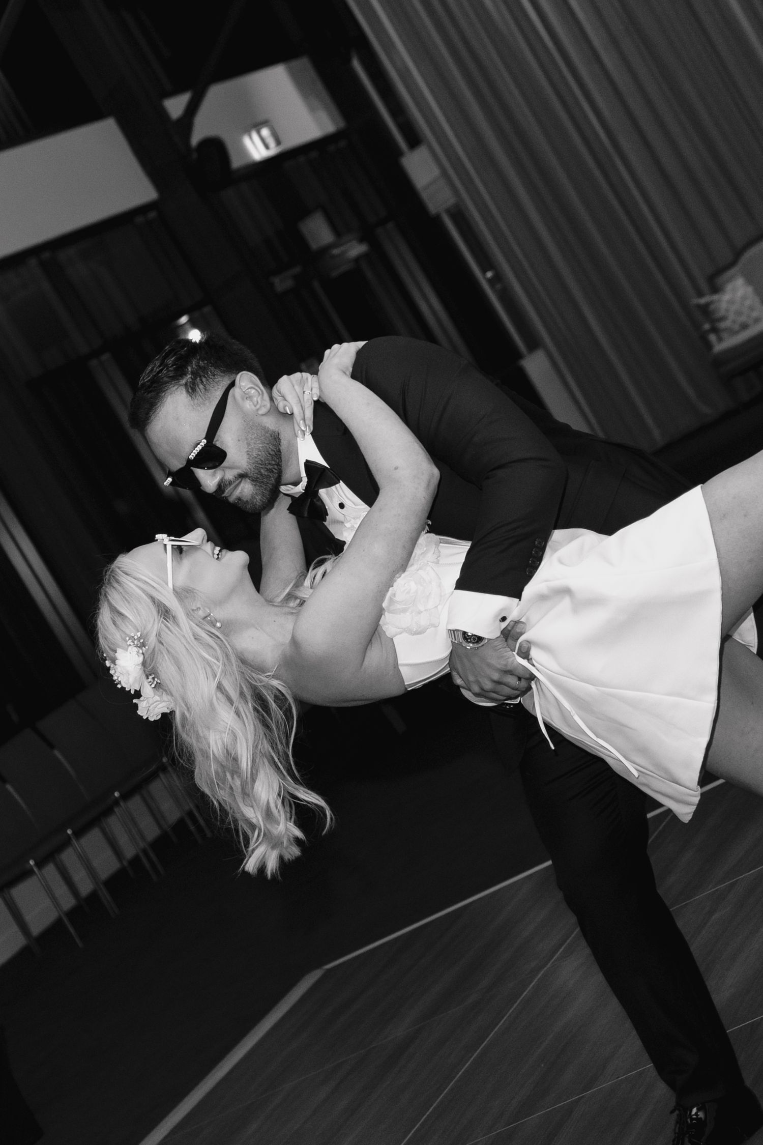 A couple performs a dramatic dance dip move during a formal dance performance on a dark stage.