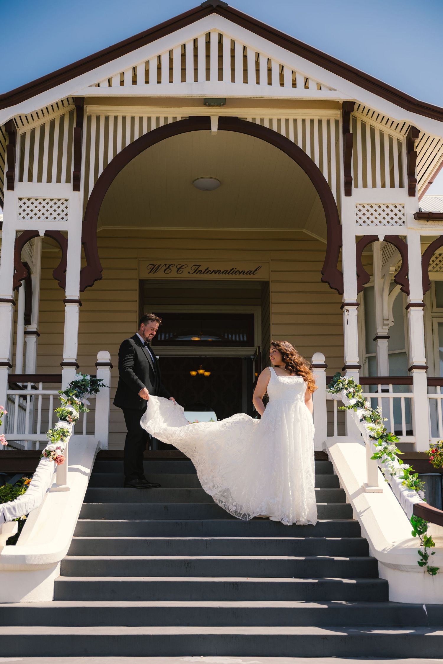 Wedding party poses on steps of a white colonial building with ornate architectural details.