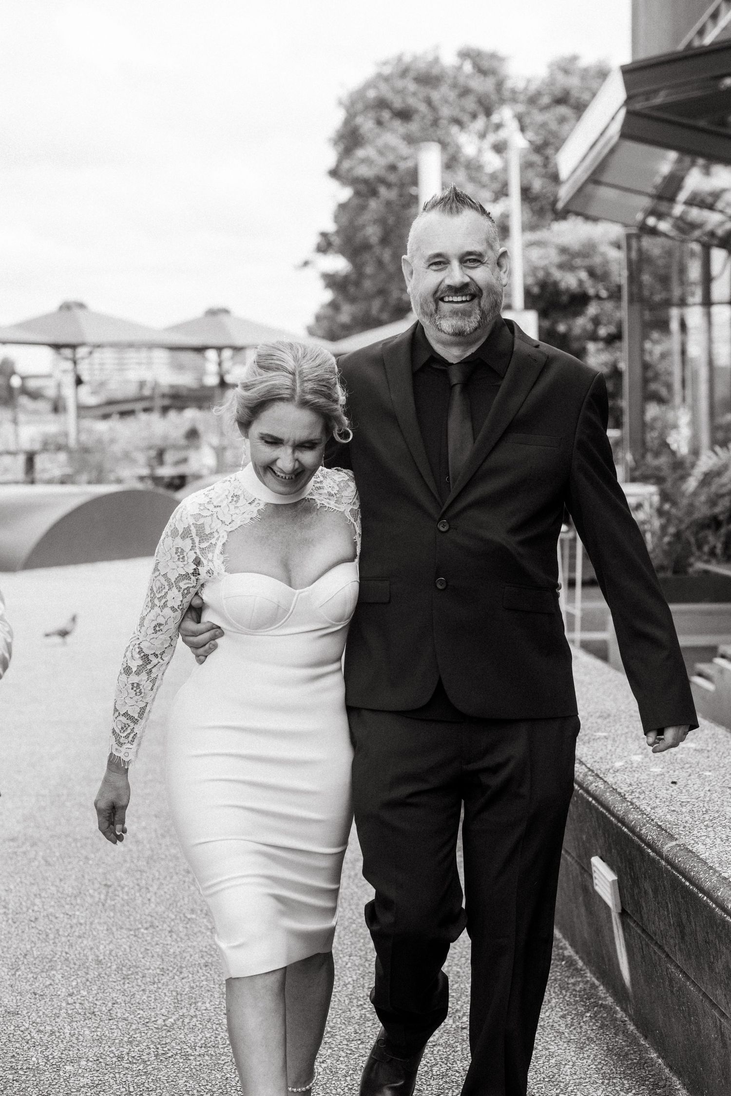 A couple in wedding attire walking and laughing together outdoors in black and white photography.