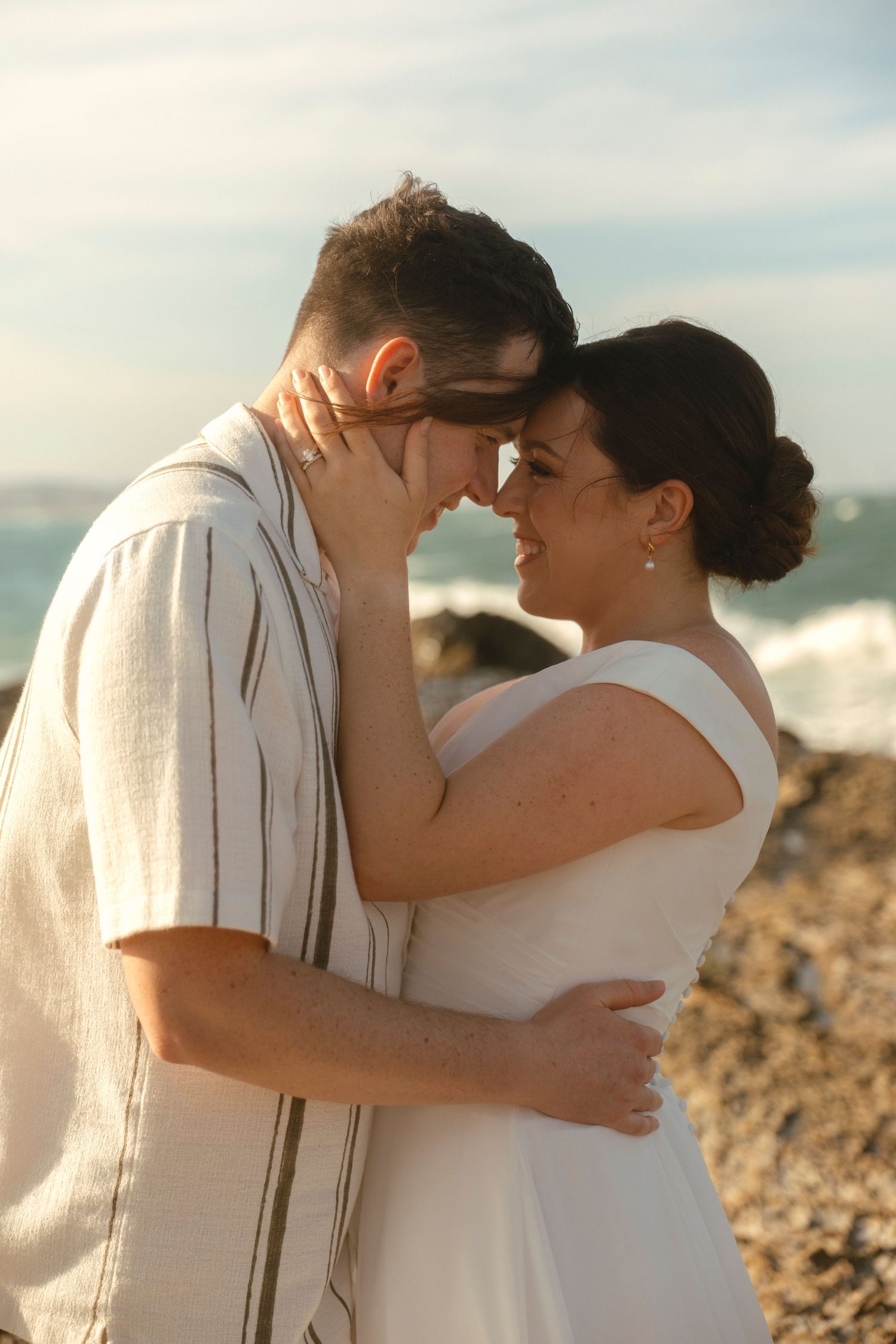 A romantic couple embraces and kisses on a rocky beach at sunset in a series of tender moments.