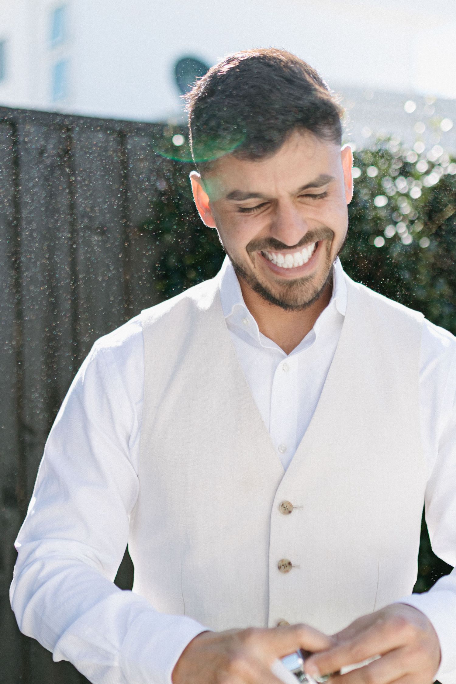 A person in a white button-up shirt smiles while looking down at their hands in a candid photo series.