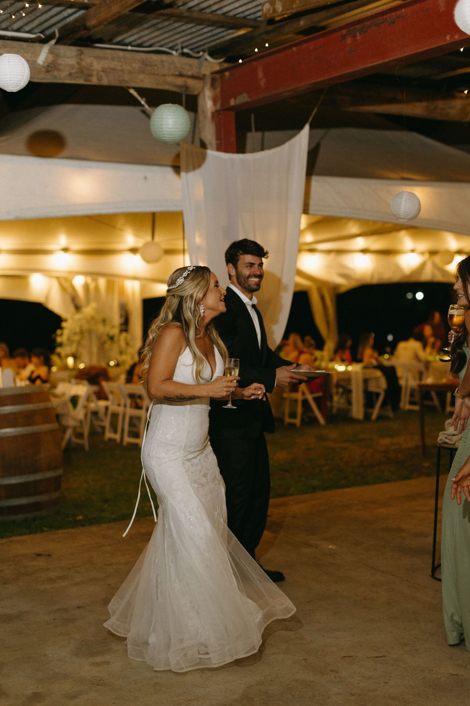 A couple shares their first dance under warm lighting at an outdoor wedding reception.