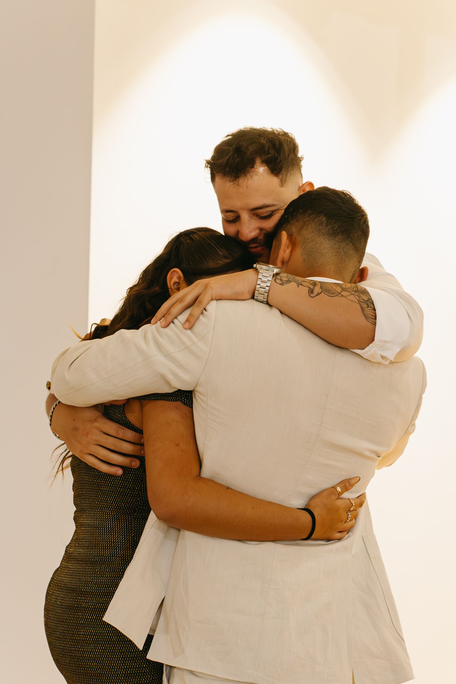Three people share a warm group hug while wearing formal attire.