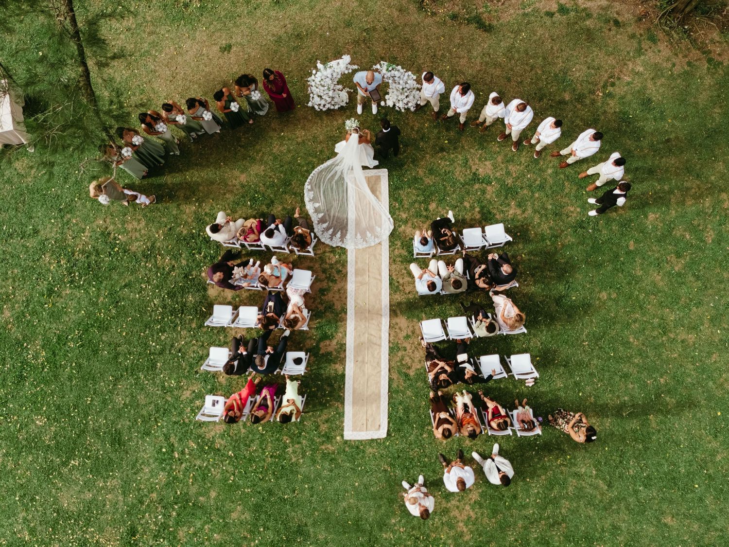 Aerial view of outdoor wedding ceremony setup with white chairs arranged on green lawn.