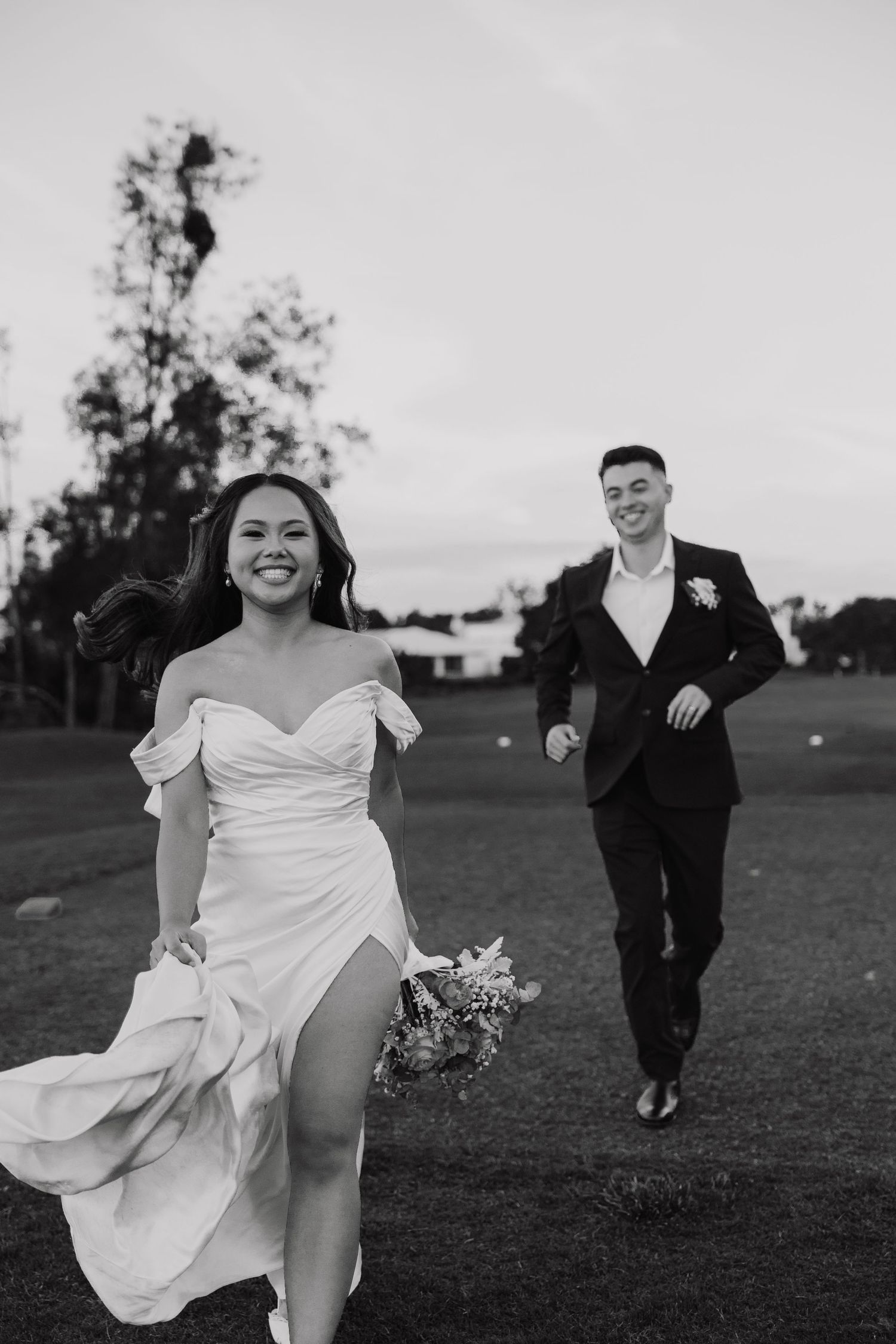 Black and white wedding photos showing playful moments between newlyweds running in a grassy field at sunset.