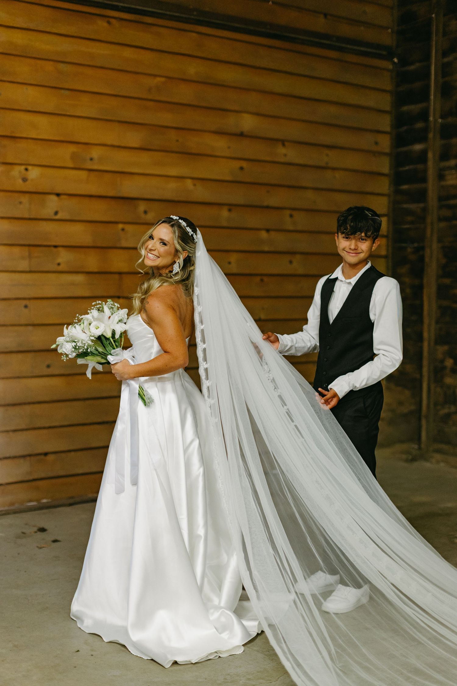 A flowing white wedding dress train being arranged in a rustic wooden barn setting.