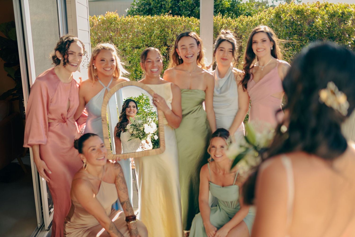 A wedding party laughs together during a joyful outdoor celebration in pink and yellow attire.
