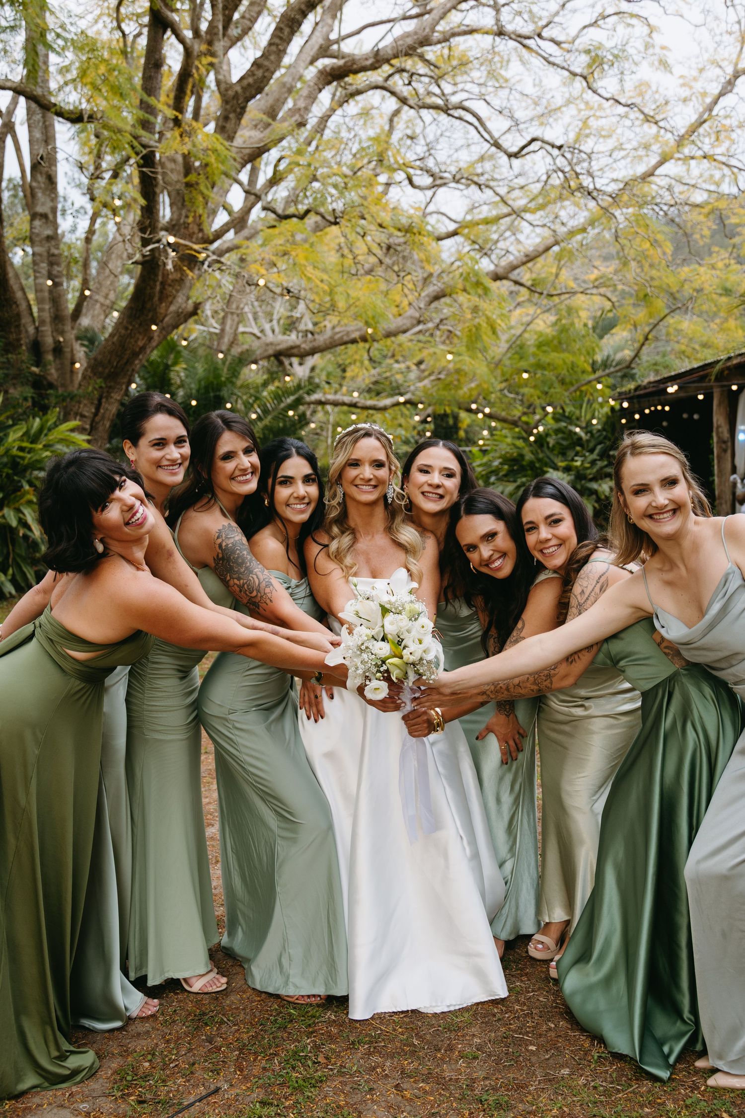 Wedding party in sage green dresses poses creatively under autumn trees.